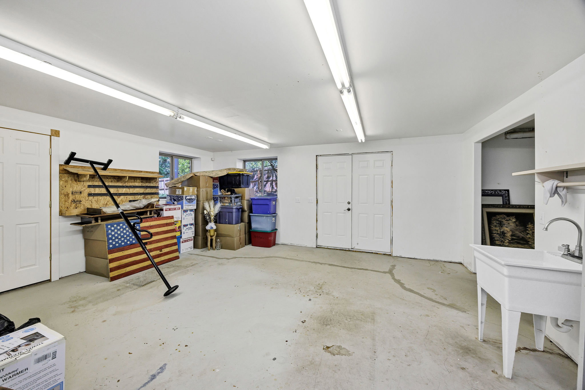 Spacious utility room featuring white walls, concrete flooring, multiple fluorescent lighting fixtures, and a utility sink with a chrome faucet