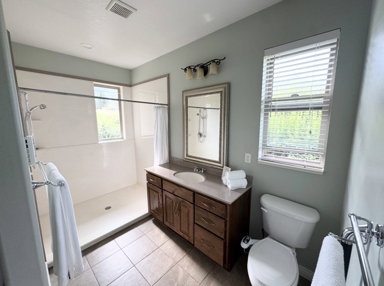 Bathroom featuring a walk-in shower with a window, a wood-finish vanity with an integrated sink, a framed mirror, and tiled flooring