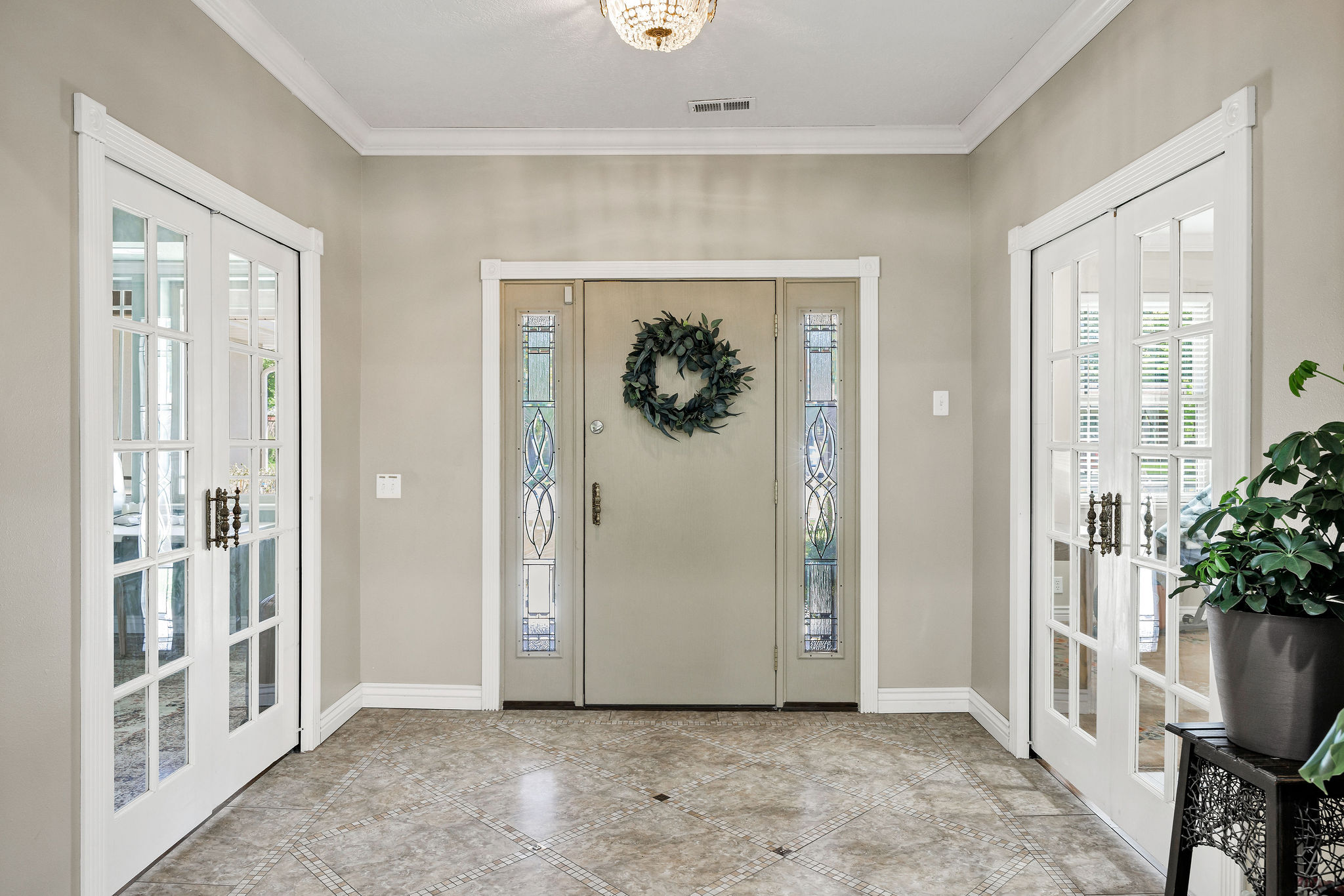 Foyer with patterned tile flooring, a central entry door with decorative glass sidelights, and two sets of interior French doors