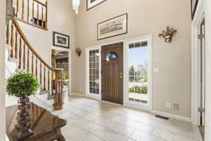 Entryway featuring a grand staircase with wood banister, tile flooring, a dark wood front door with an arched window, and two sidelight windows