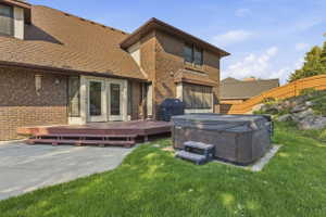Expansive outdoor space featuring a hot tub, a large multi-level wood deck, concrete patio, and a manicured lawn