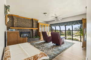 Living area featuring a floor-to-ceiling curved window wall, a brick-surround fireplace with a wood mantle, wood-finish flooring, a ceiling fan, and built-in wood cabinetry