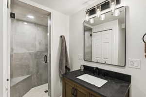 Bathroom featuring a glass-enclosed shower with a built-in bench, wood-finish vanity with an undermount sink, dark stone countertop, and matte black fixtures