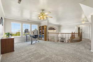 Carpeted loft area featuring a curved wood banister, three large windows, a built-in wood bookshelf, and a ceiling fan light fixture