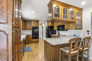 Kitchen featuring wood cabinetry, light-toned countertops, a full suite of black appliances, recessed lighting, and wood-finish flooring