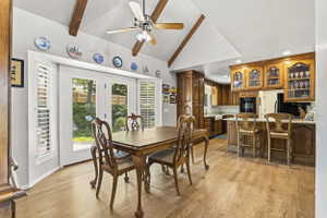 Open-concept dining area with vaulted ceilings featuring exposed wood beams and a ceiling fan
