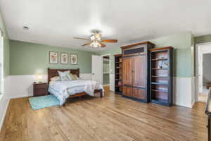 Spacious room featuring wood-finish flooring, half-wall beadboard paneling, and a ceiling fan with integrated lighting