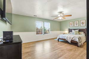 Spacious room featuring wood-finish flooring, two large windows, white wainscoting, a ceiling fan, and ample wall space