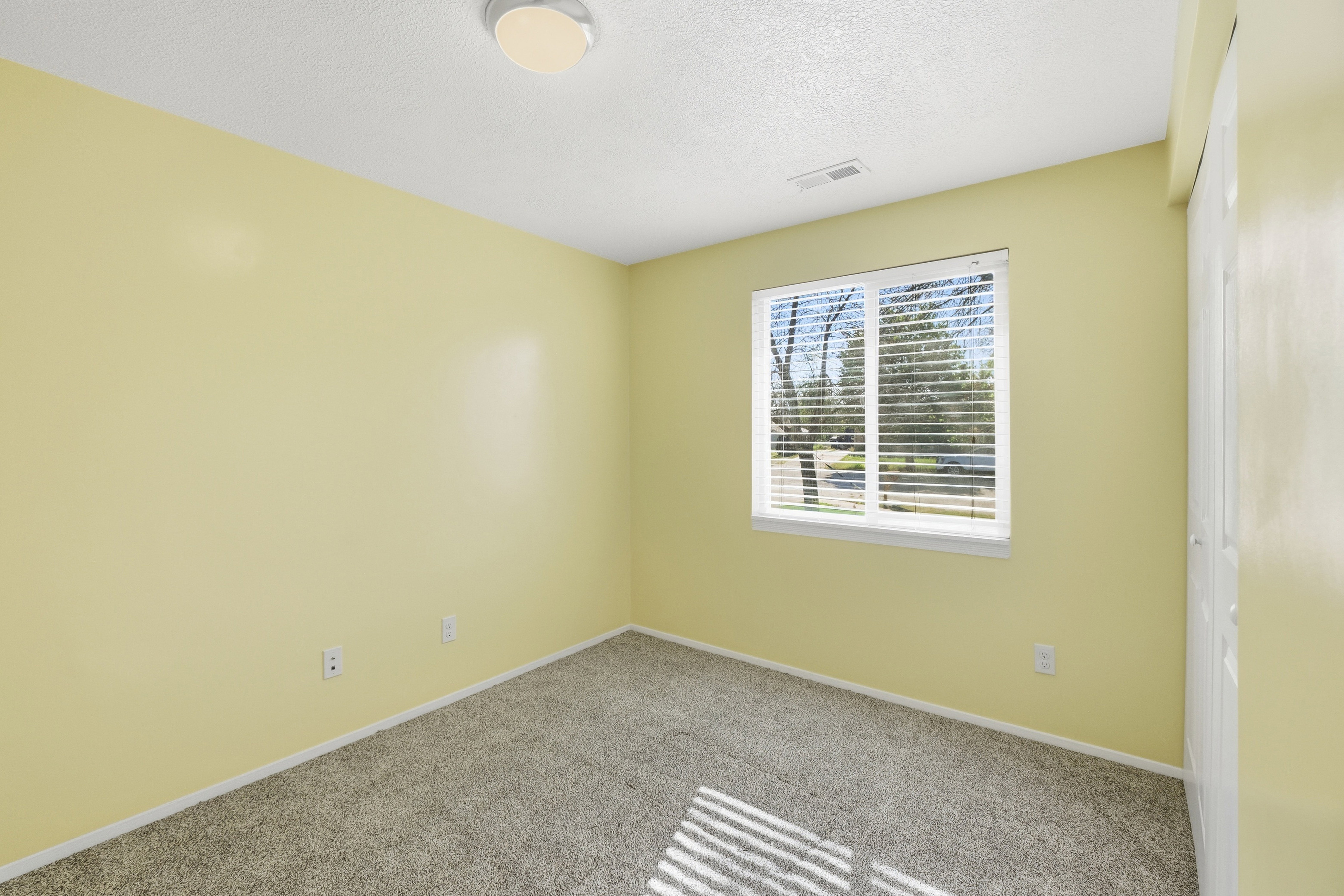 Carpeted room featuring a window with blinds, a ceiling-mounted light fixture, and a built-in closet with bifold doors