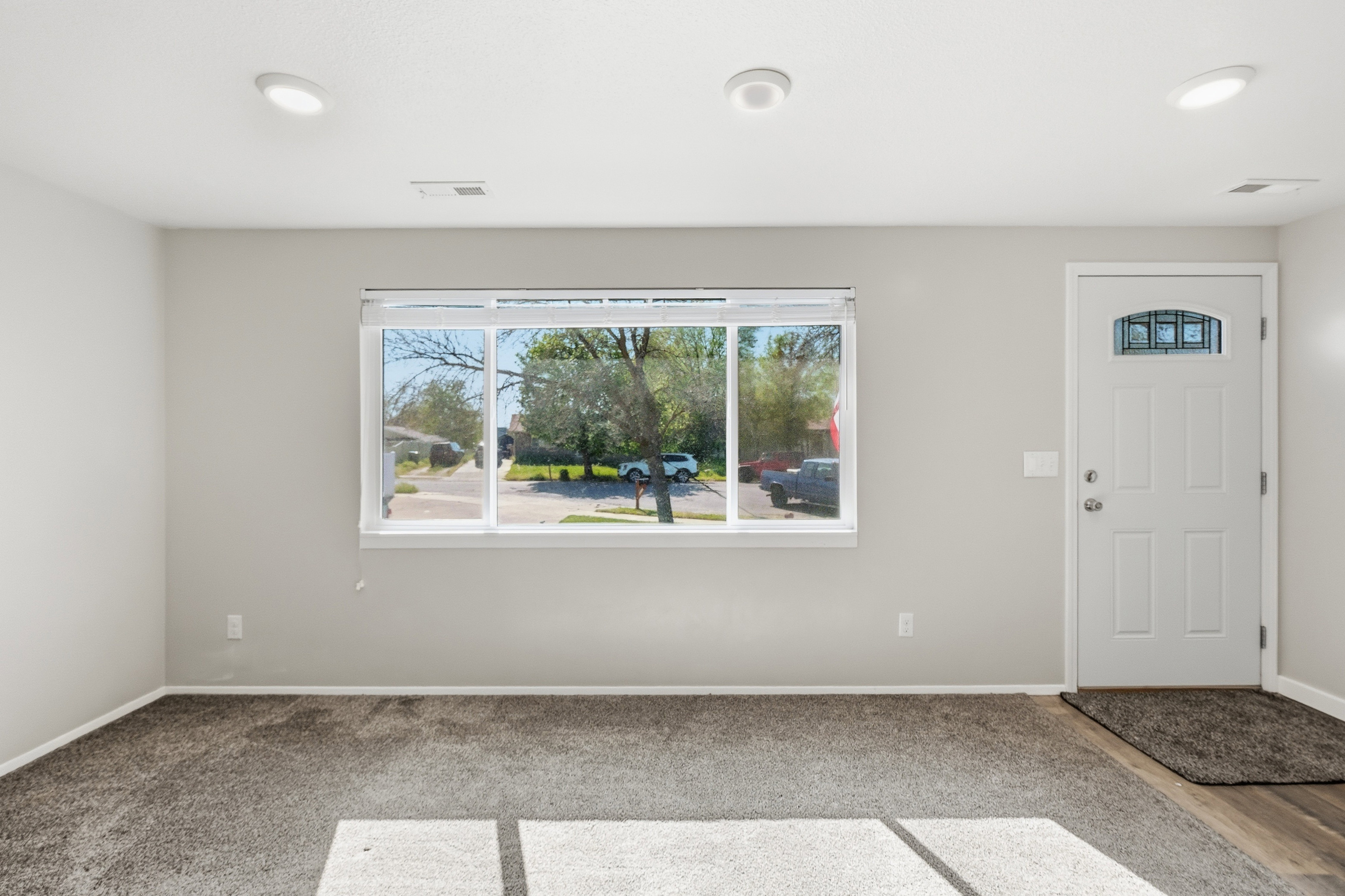 Spacious entry area with light gray walls, dark gray carpeting, and a contrasting wood-finish flooring at the entryway