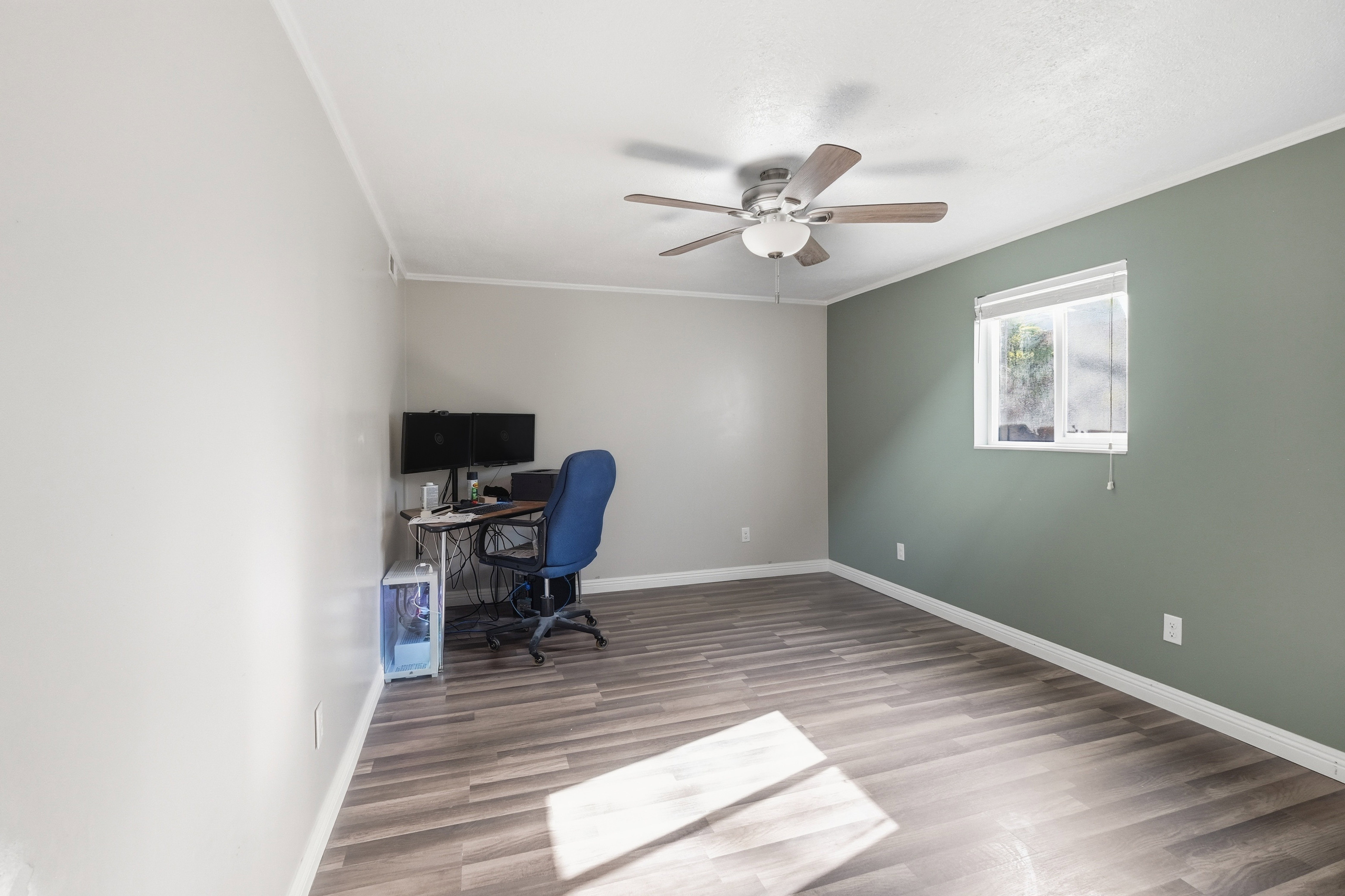 Spacious room featuring wood-finish flooring, a ceiling fan, and a window with blinds