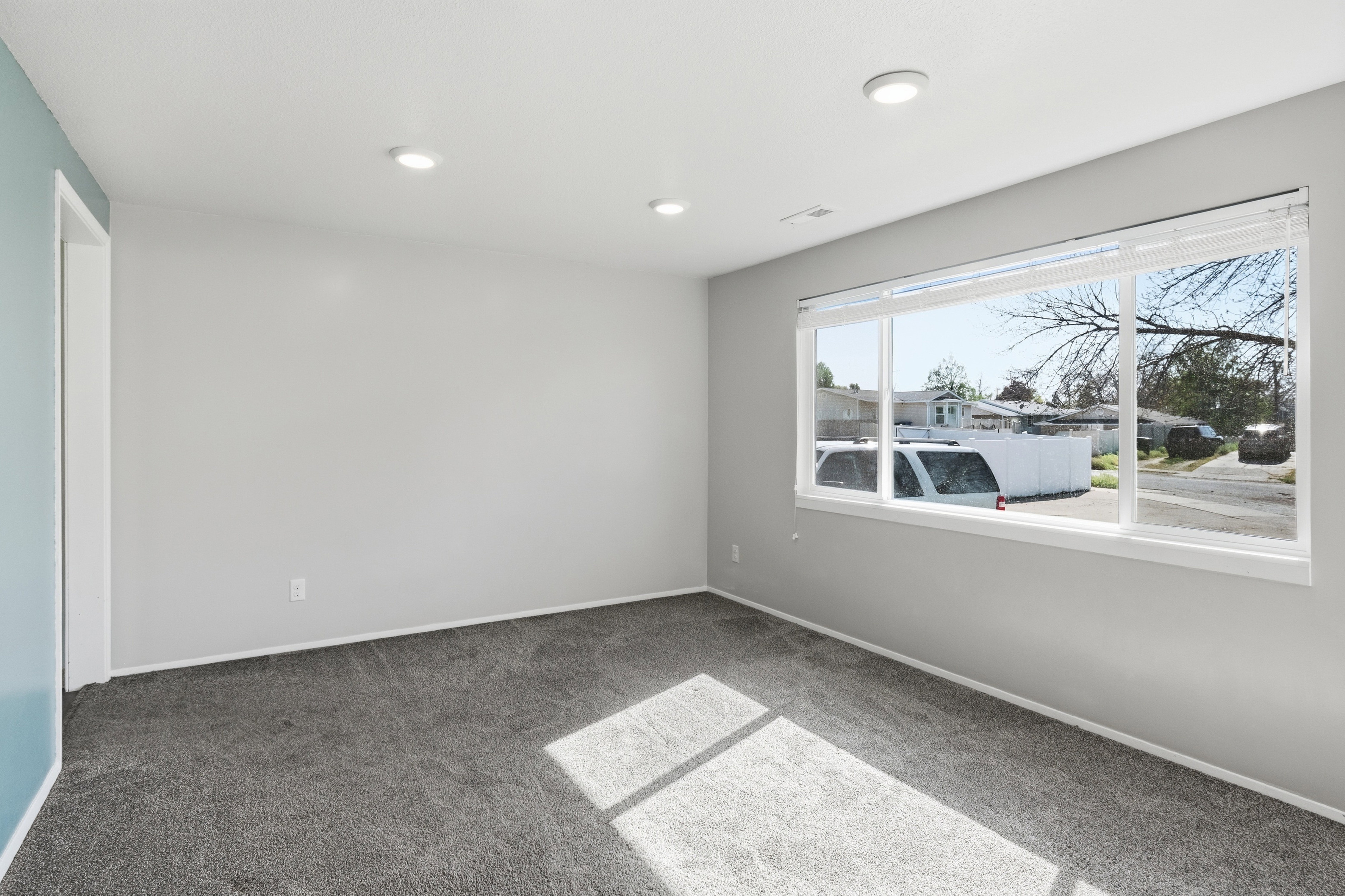 Recessed ceiling lighting, light gray wall paint, contrasting accent wall, gray carpet flooring, and a large window with white blinds