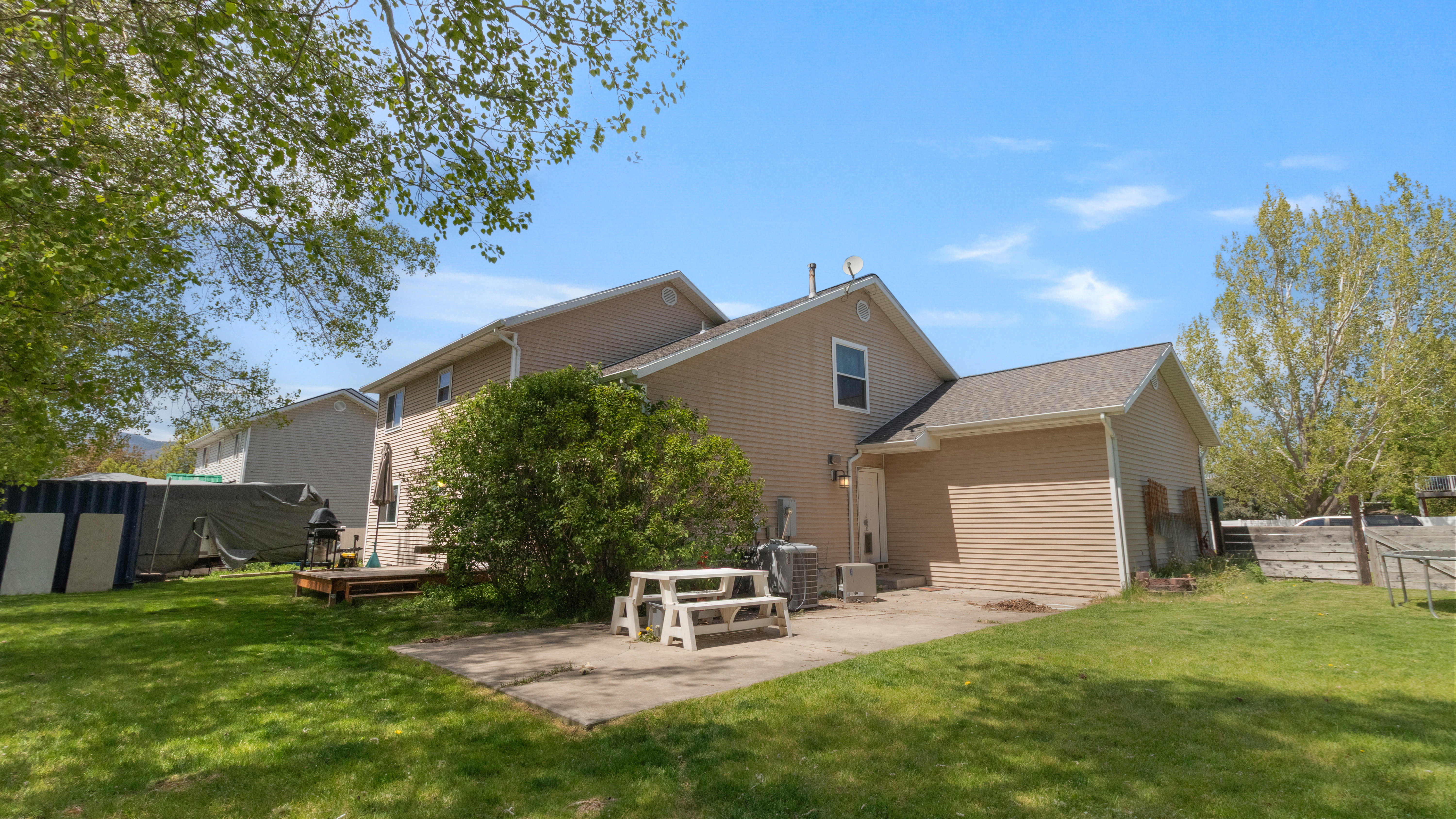 Expansive rear yard featuring a concrete patio, wood deck, and lush green lawn