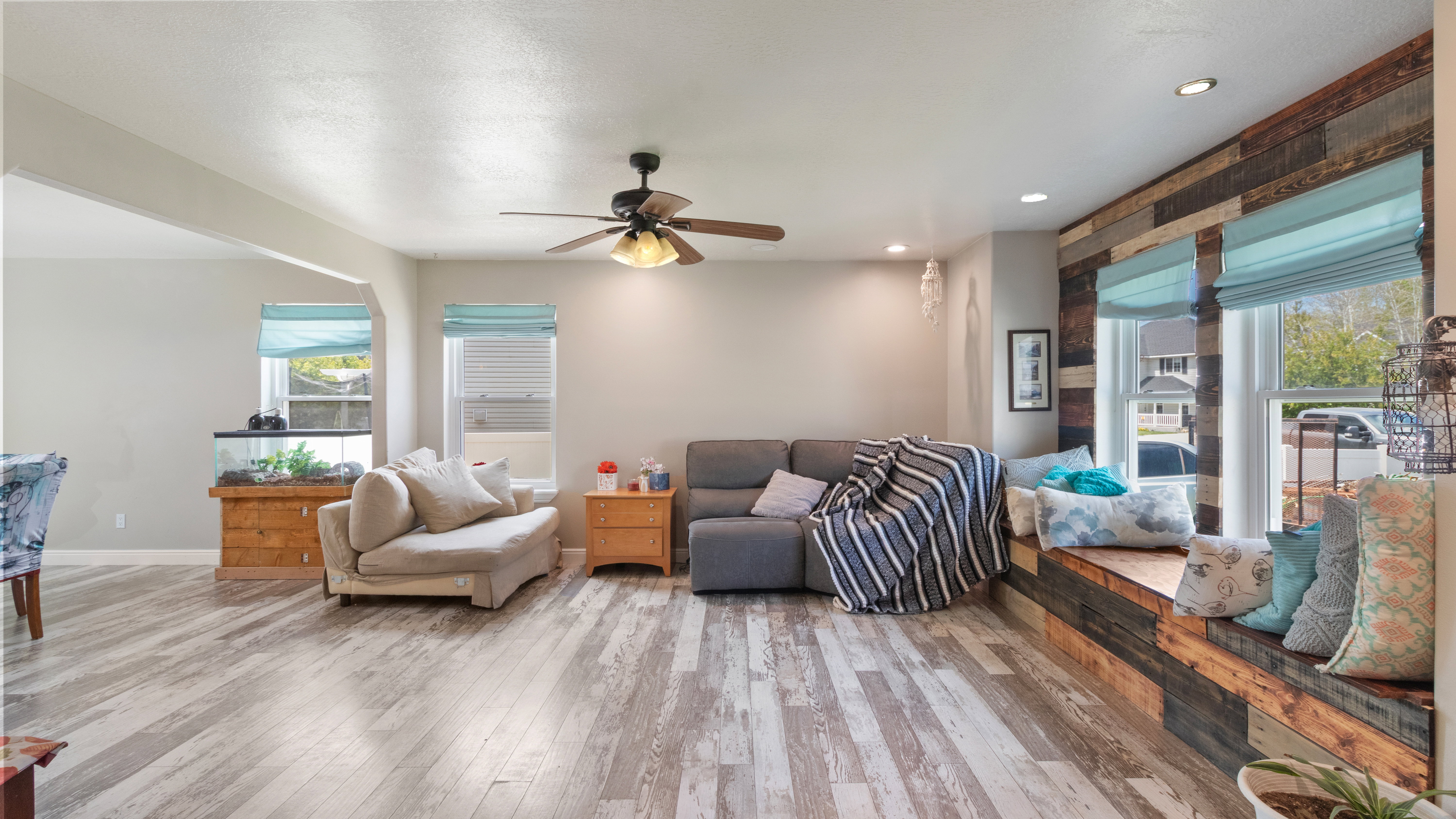 Spacious room featuring wood-finish flooring, a built-in window seat with a wood-plank accent wall, recessed lighting, and a ceiling fan