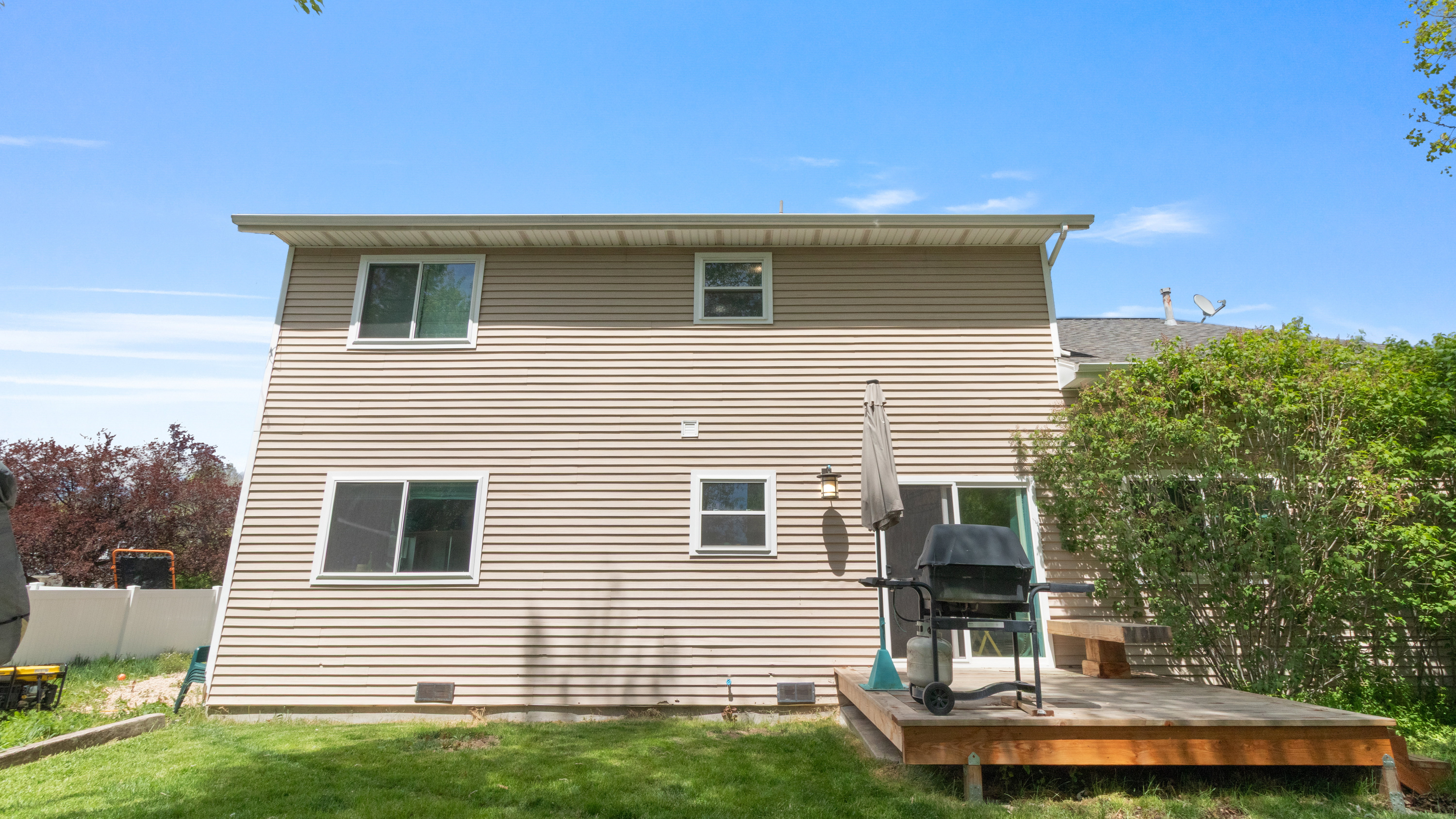 Rear exterior featuring beige siding, multiple windows, and a ground-level wood deck