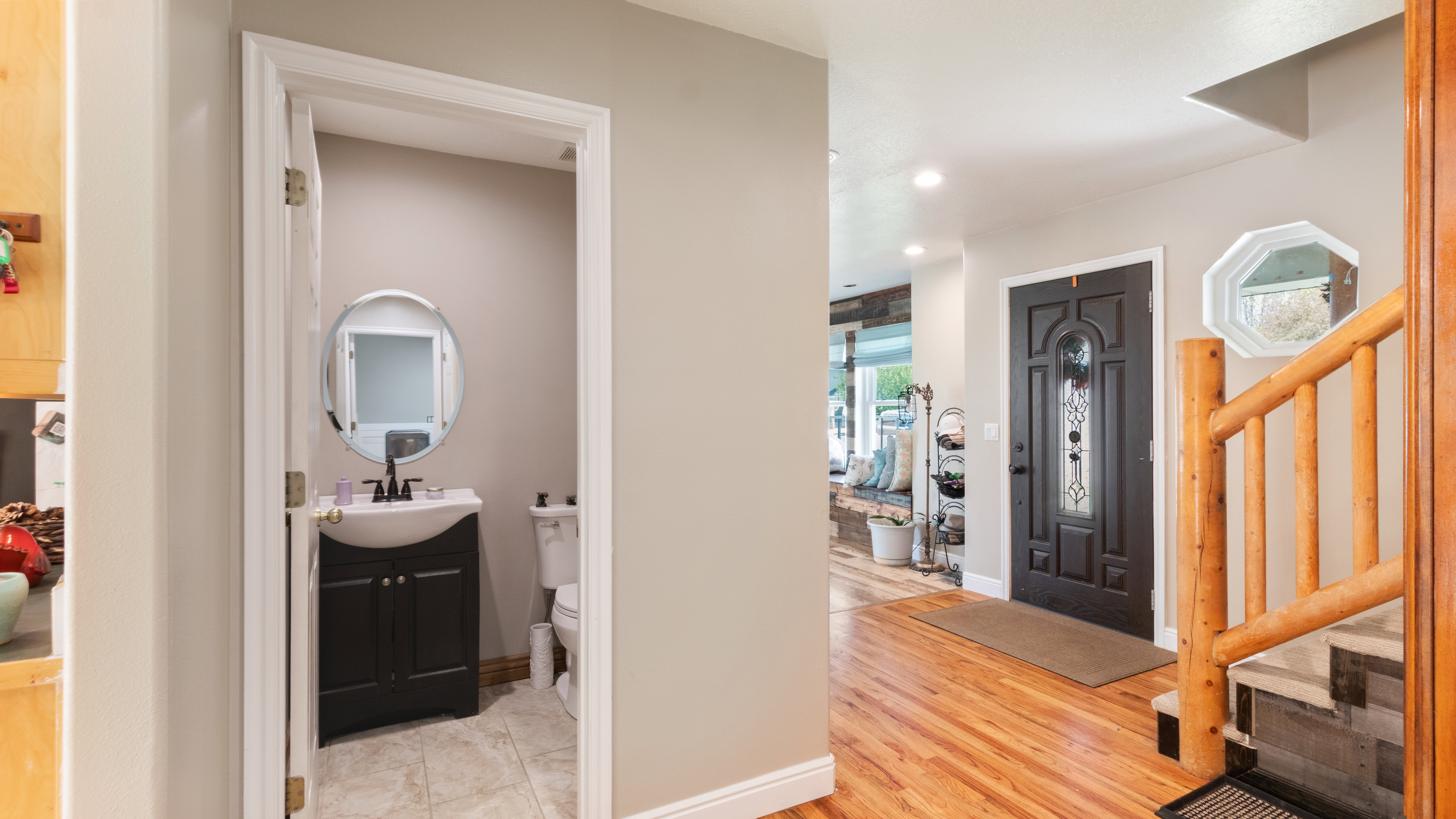 Hardwood flooring extending through the entry, with a wood-finish staircase railing, and a dark paneled front door featuring decorative glass