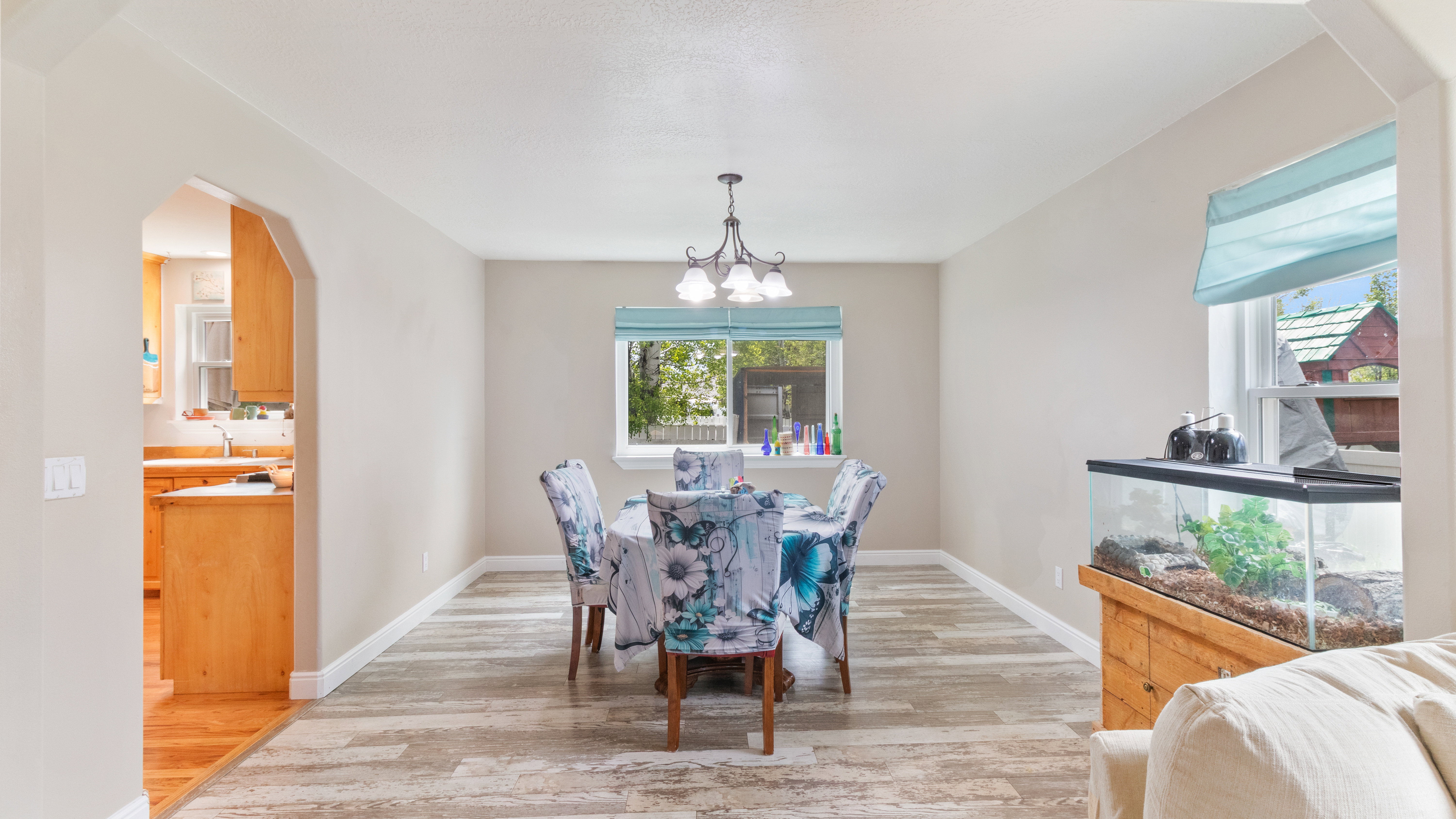 Dining area featuring wood-finish flooring, a central window with a light blue Roman shade, and a multi-bulb chandelier