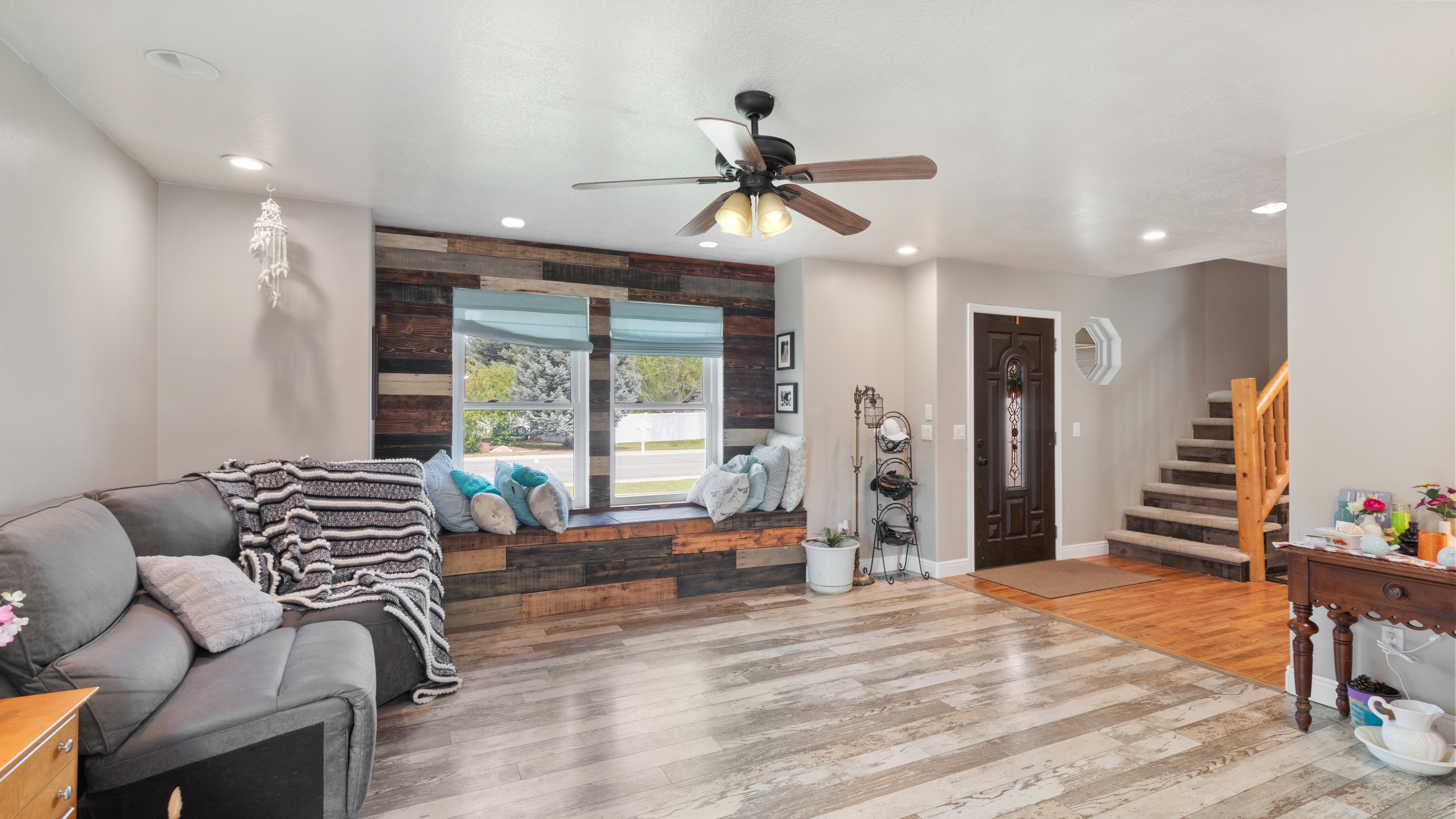 Spacious living area featuring a wood-finish accent wall with an integrated window seat, multi-tone wood-finish flooring, recessed lighting, and a ceiling fan
