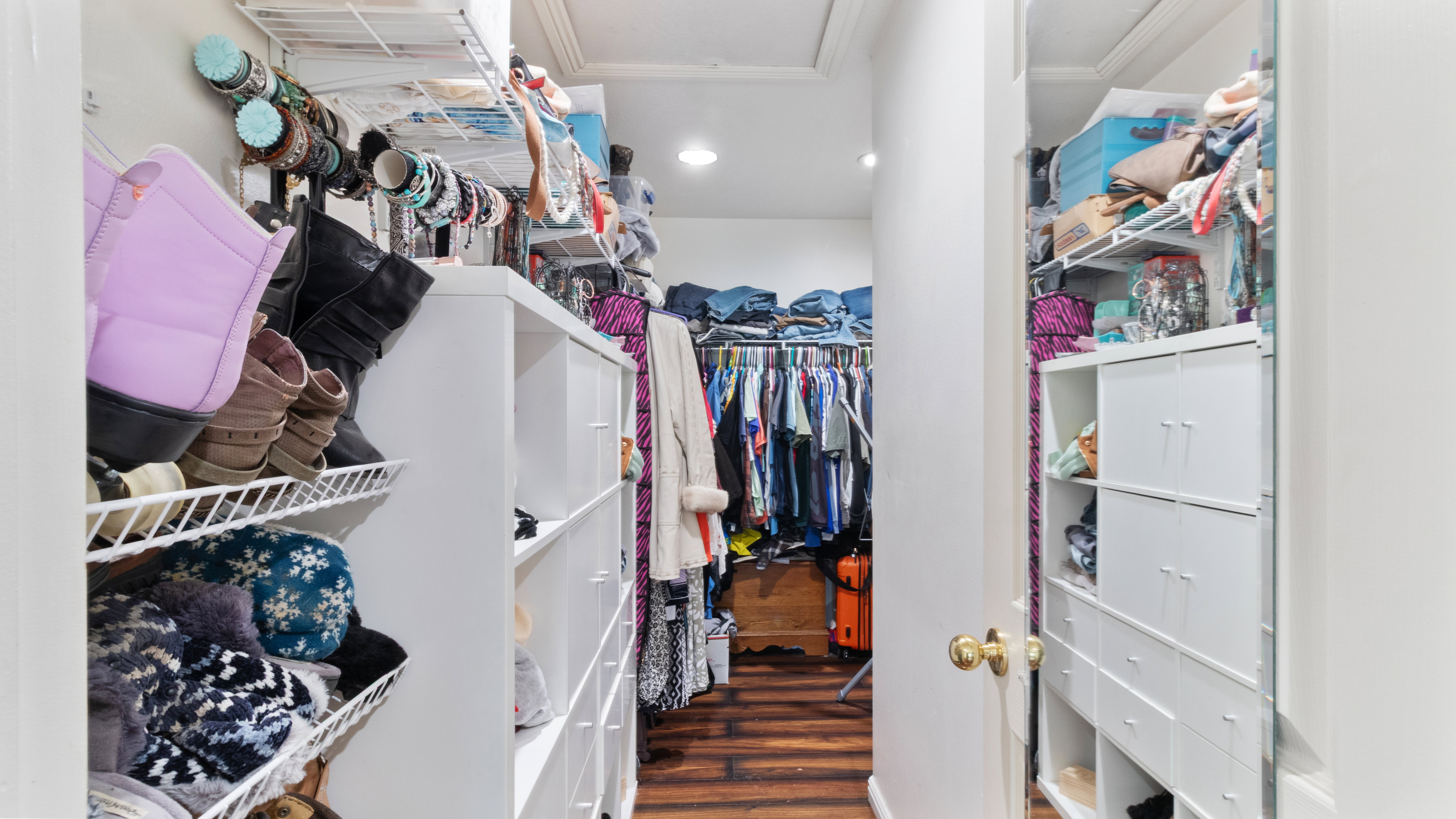 Walk-in closet featuring wood-finish flooring, recessed lighting, and extensive custom storage solutions including open shelving, wire racks, and built-in drawers