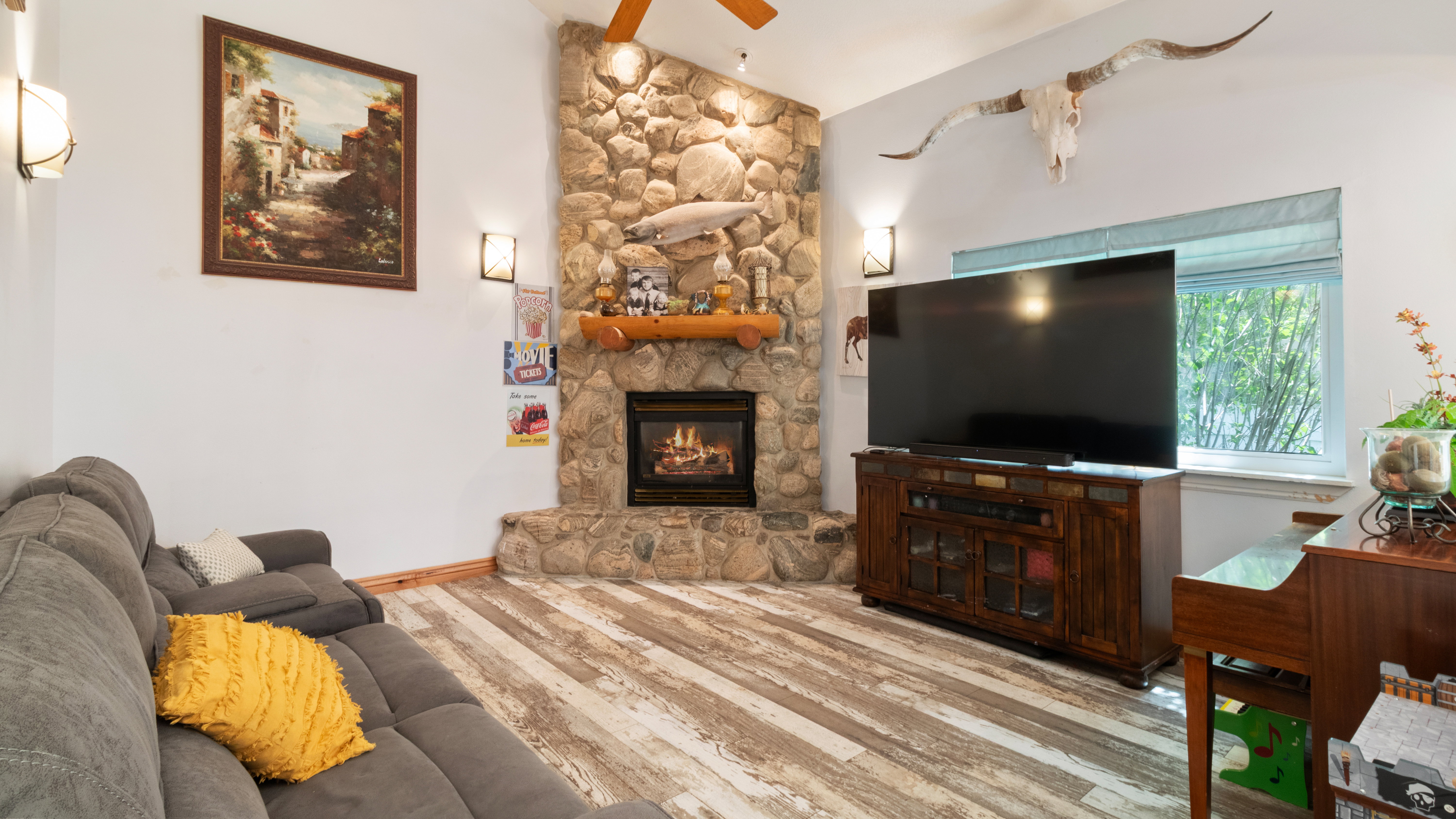 Vaulted ceiling living space featuring a stone fireplace with a wood mantle, wood-finish flooring, and wall-mounted sconces