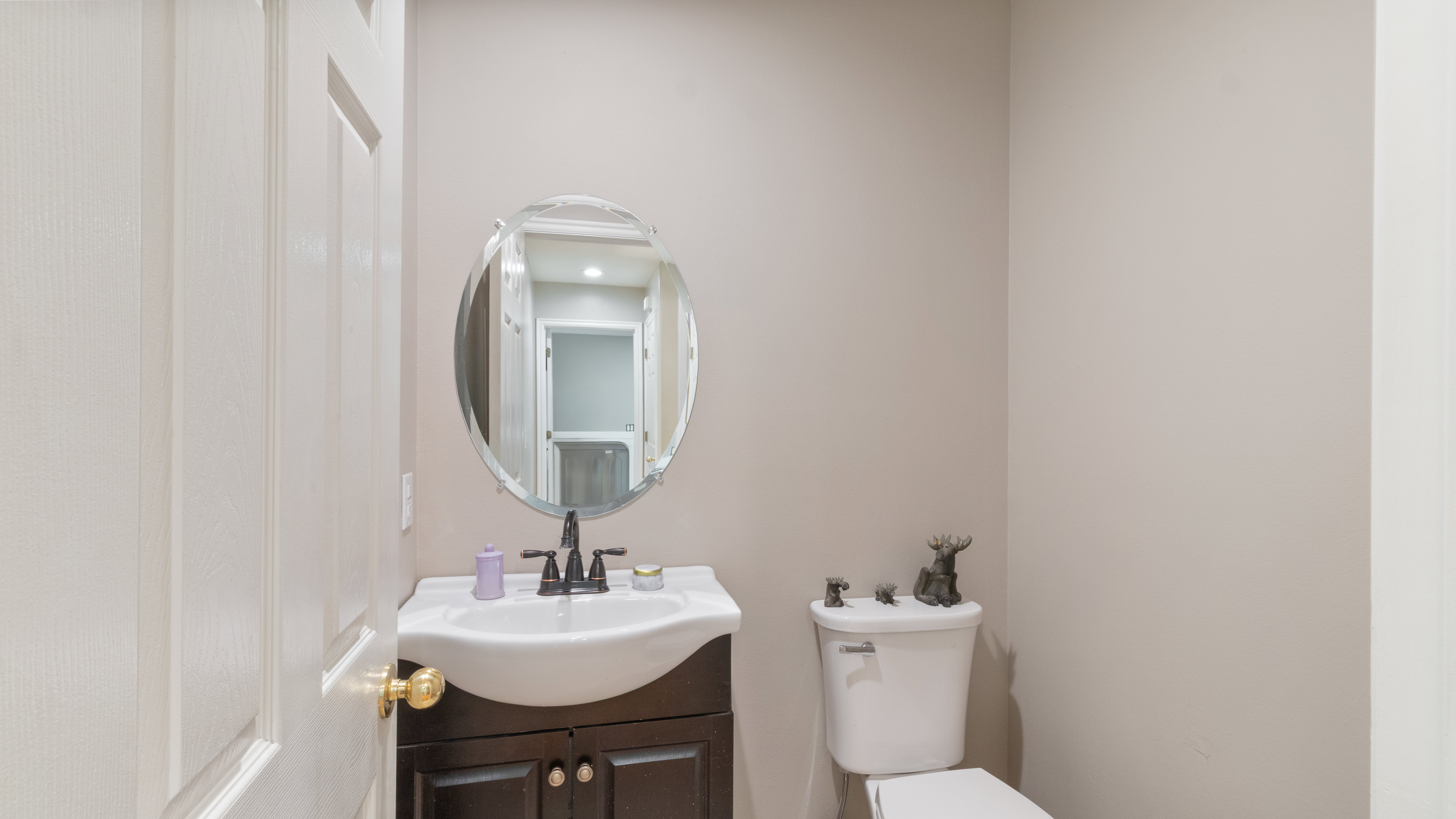 Powder room featuring a dark wood vanity with a white basin sink, an oval wall-mounted mirror, and a white toilet