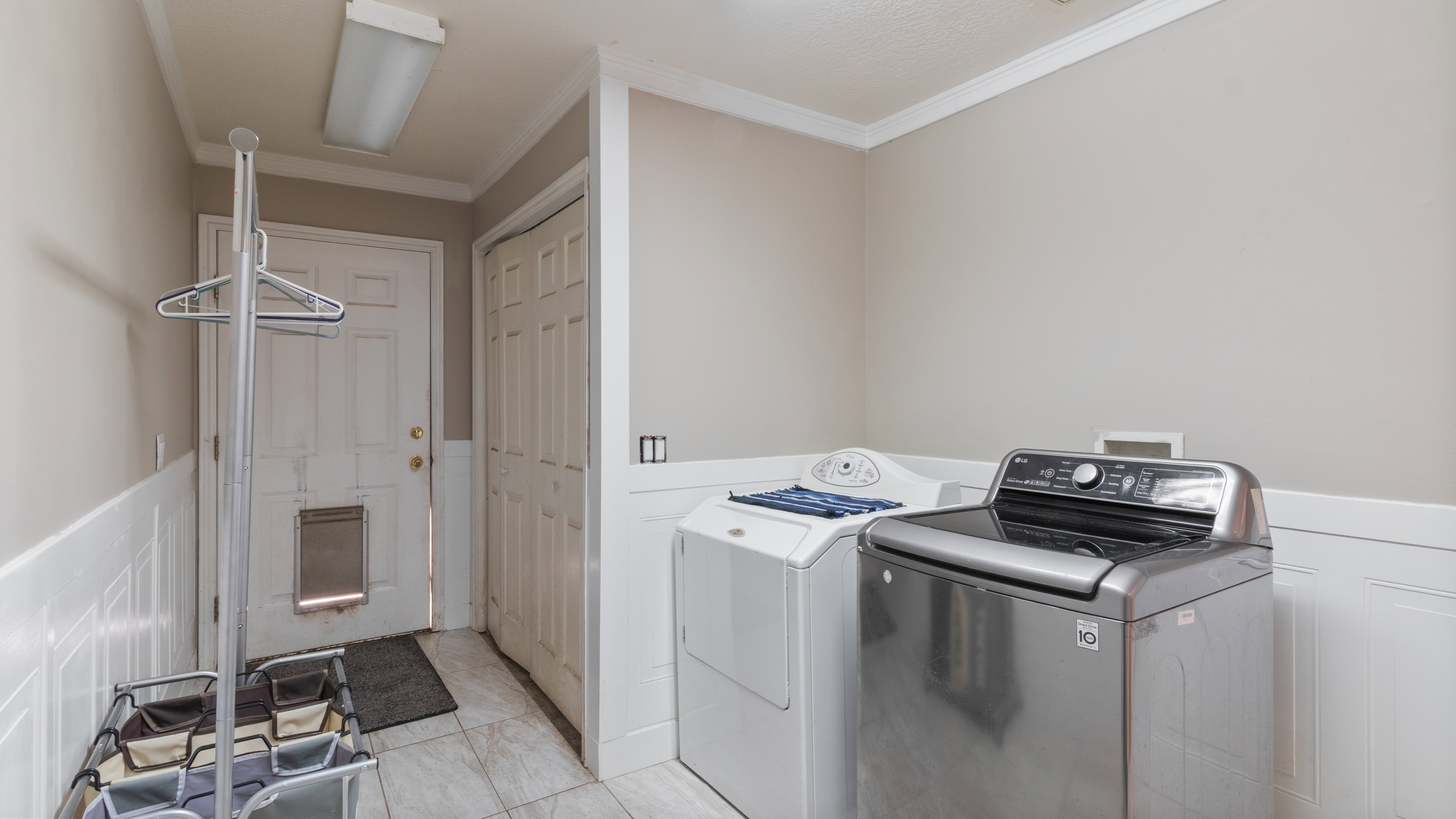Functional laundry area featuring neutral wall tones, white wainscoting, and tile flooring