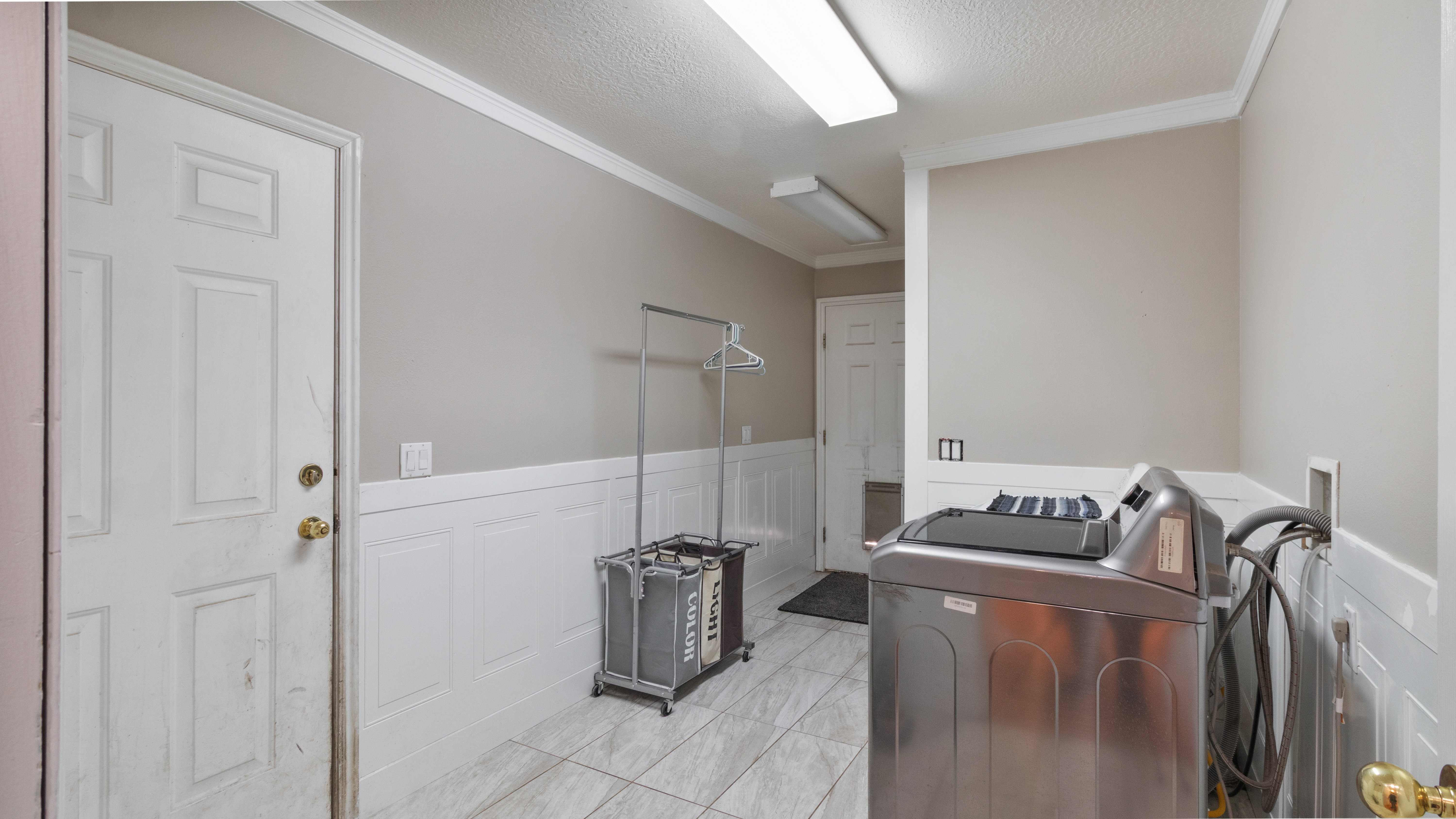 Utility room featuring wainscoting, crown molding, a panel door, and tile flooring