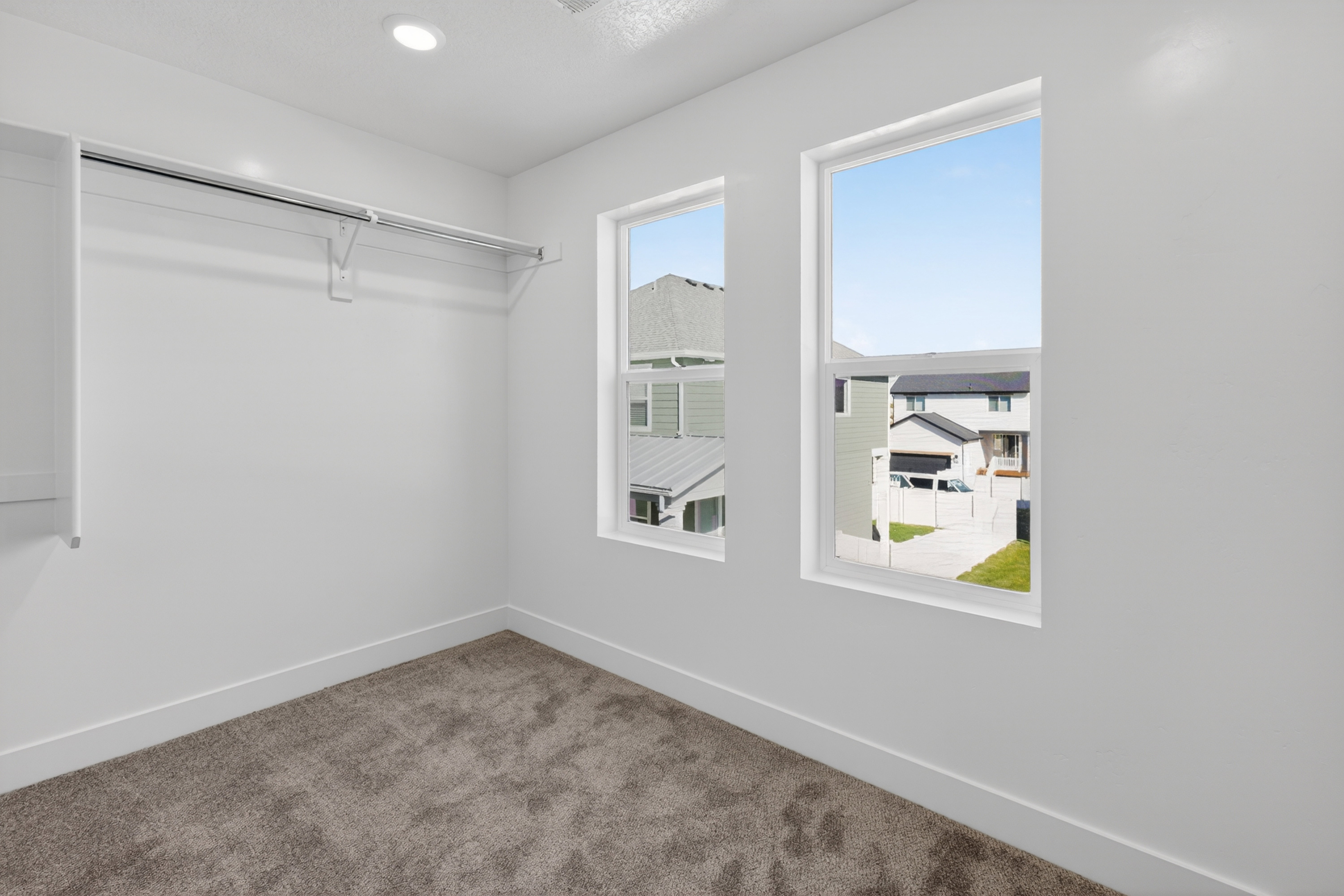 Bedroom featuring plush carpet flooring, two large windows, white walls, built-in closet shelving, and a recessed ceiling light