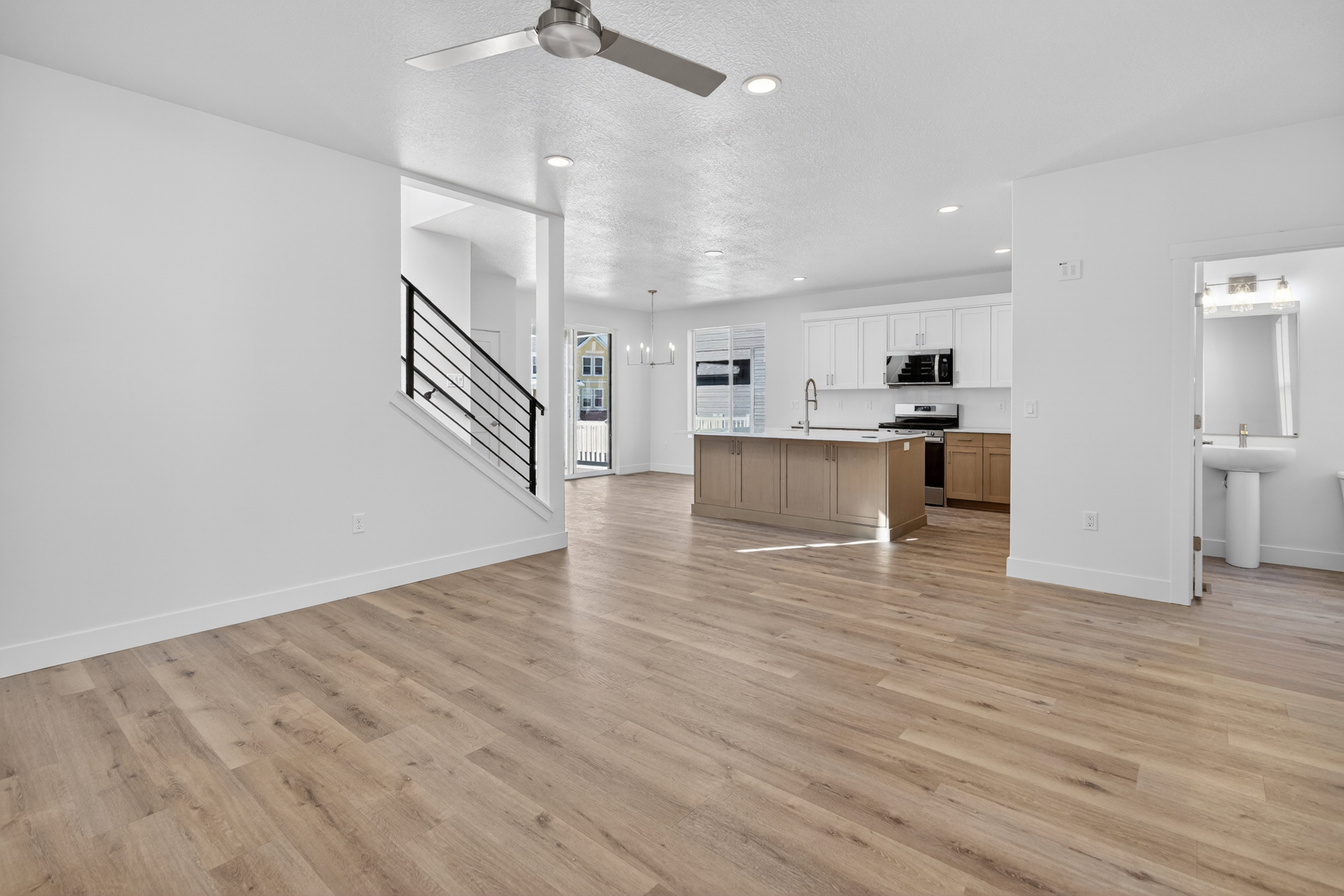 Open-concept living area featuring wood-finish flooring, a modern kitchen island with seating, white upper cabinetry, and a contemporary ceiling fan