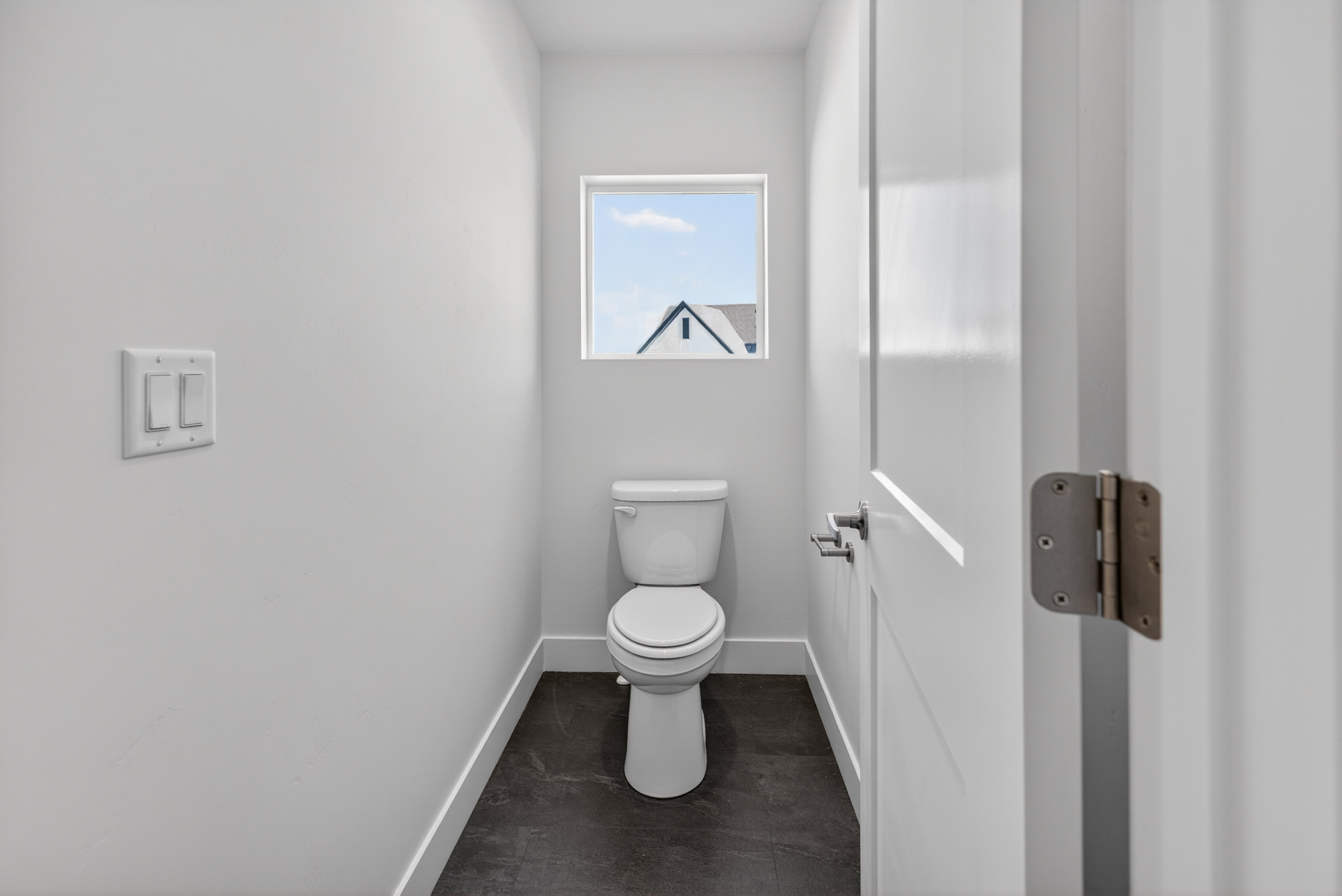 Powder room featuring a single-pane window, white toilet, dark floor tiling, and white baseboards