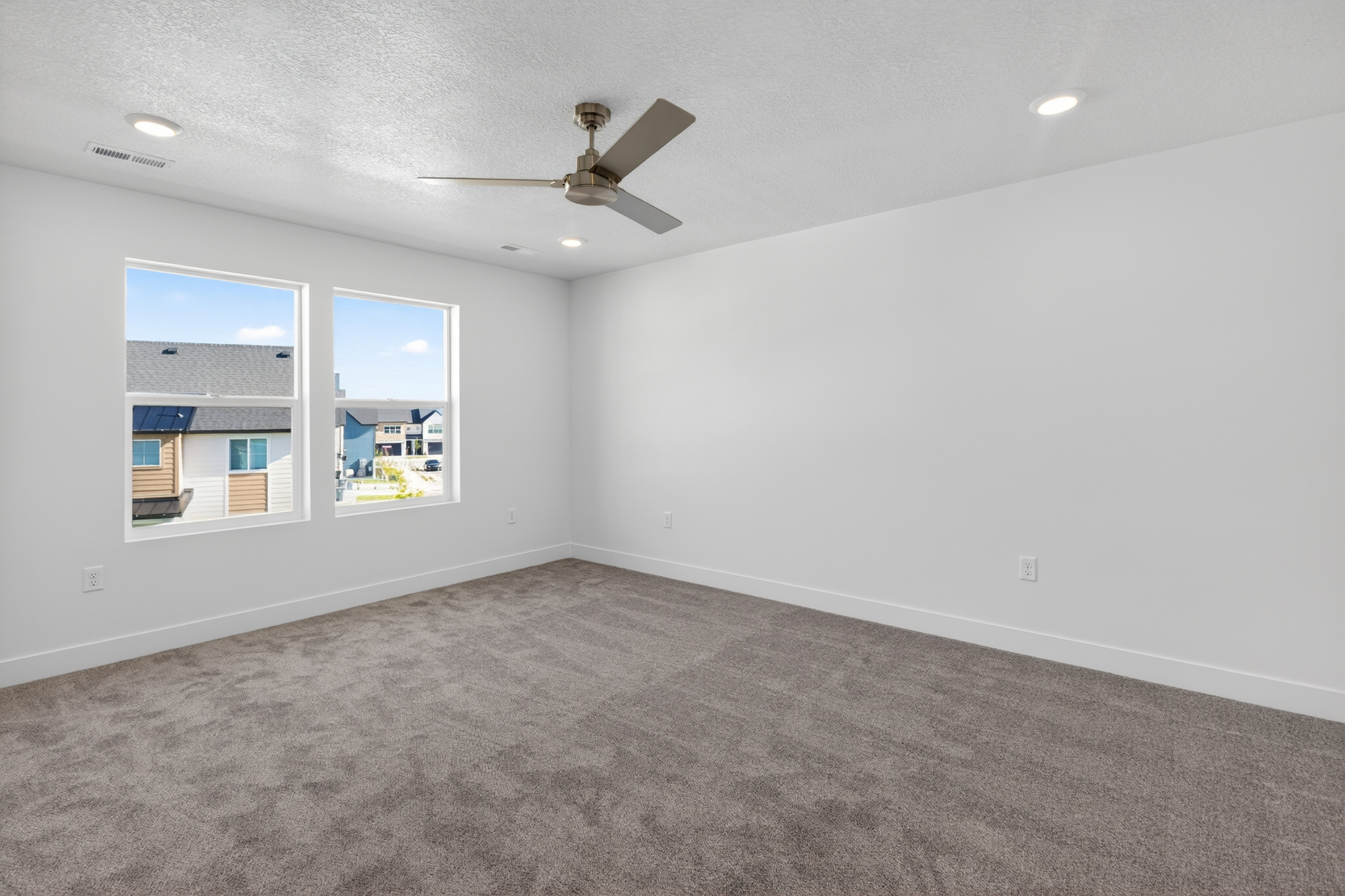 Spacious room featuring two large windows, gray carpeting, and white walls