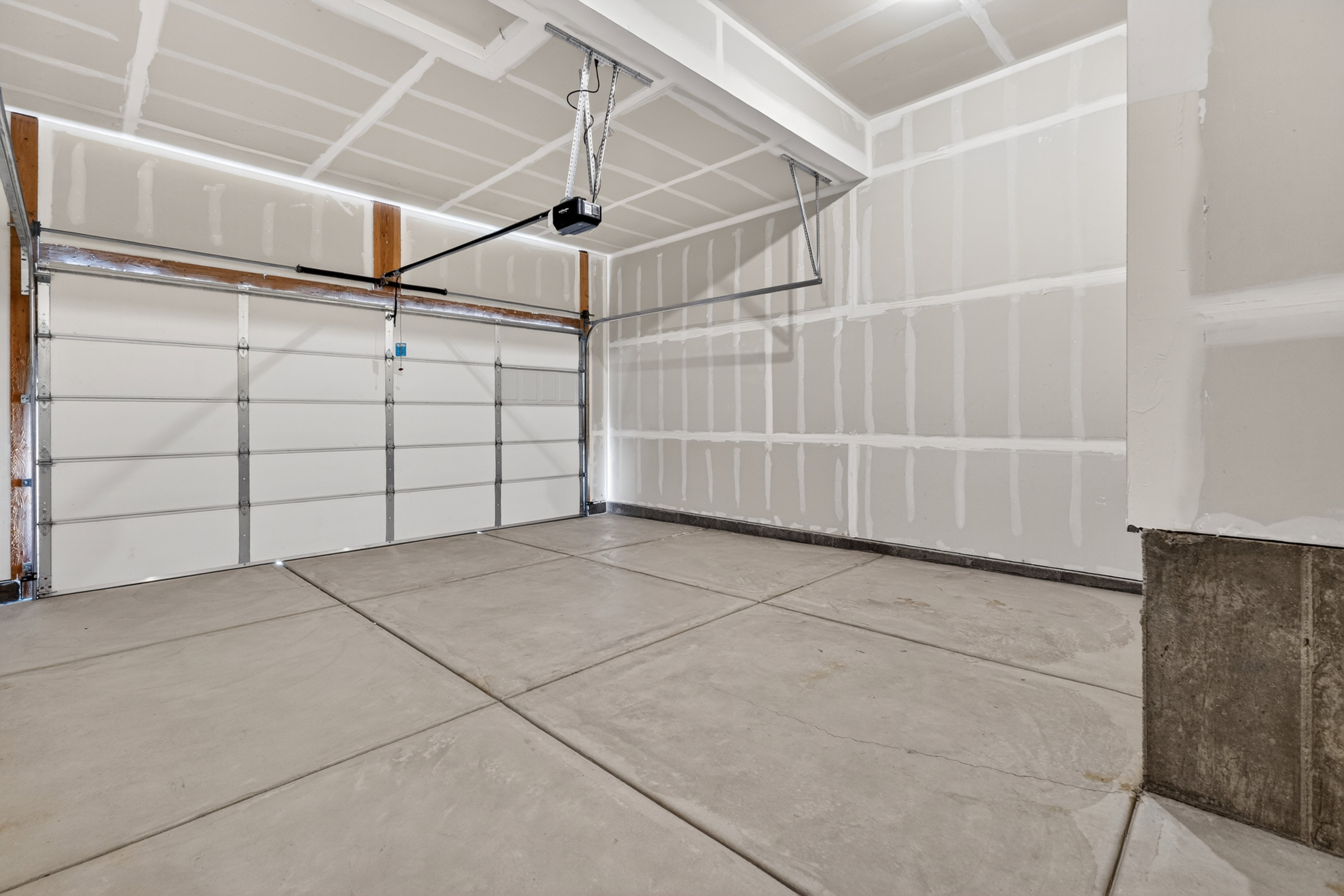 Garage featuring an automatic overhead door, concrete flooring, and unfinished drywall