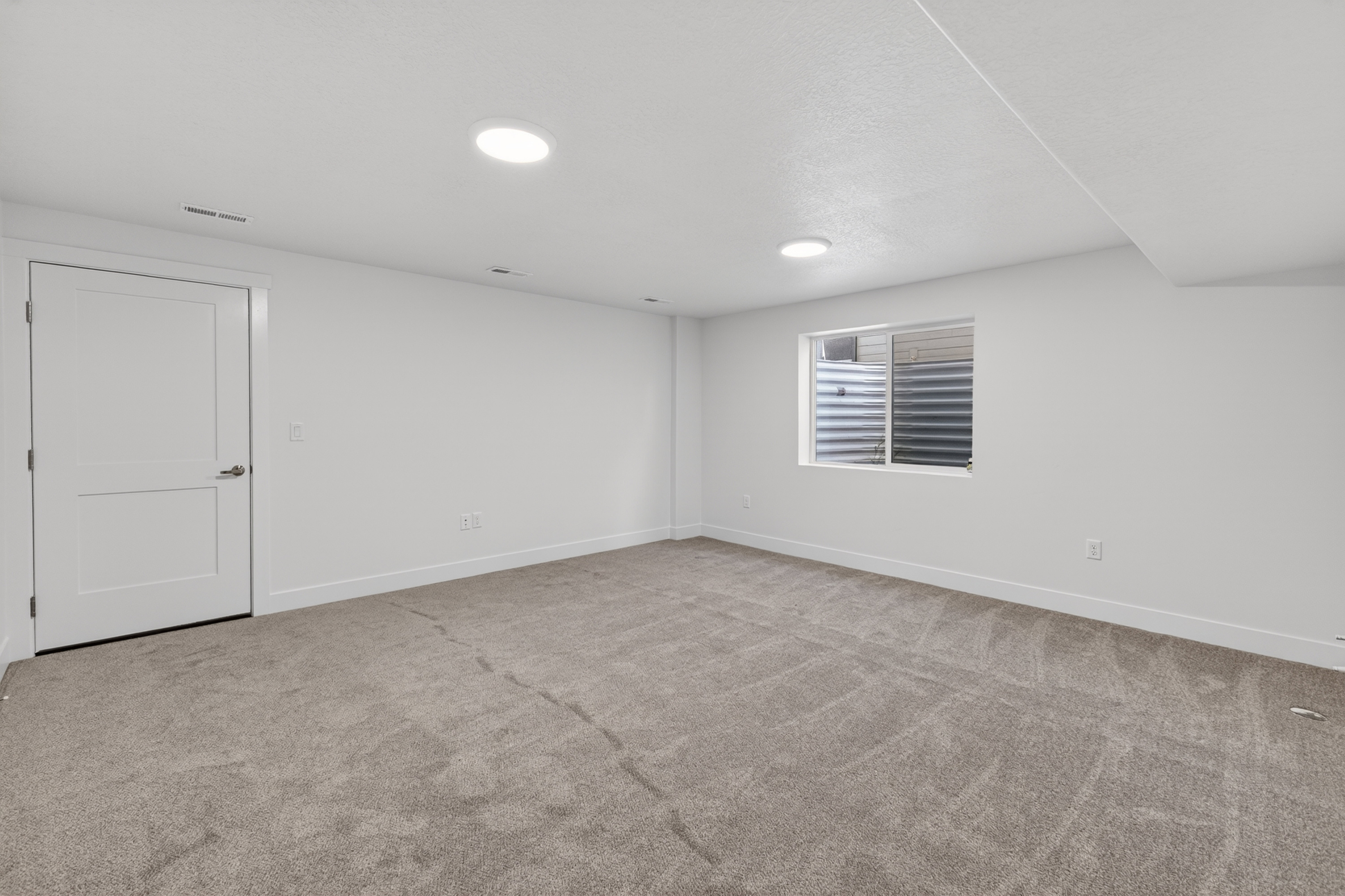 Spacious room featuring neutral carpeting, recessed lighting, white walls, and a window with security bars