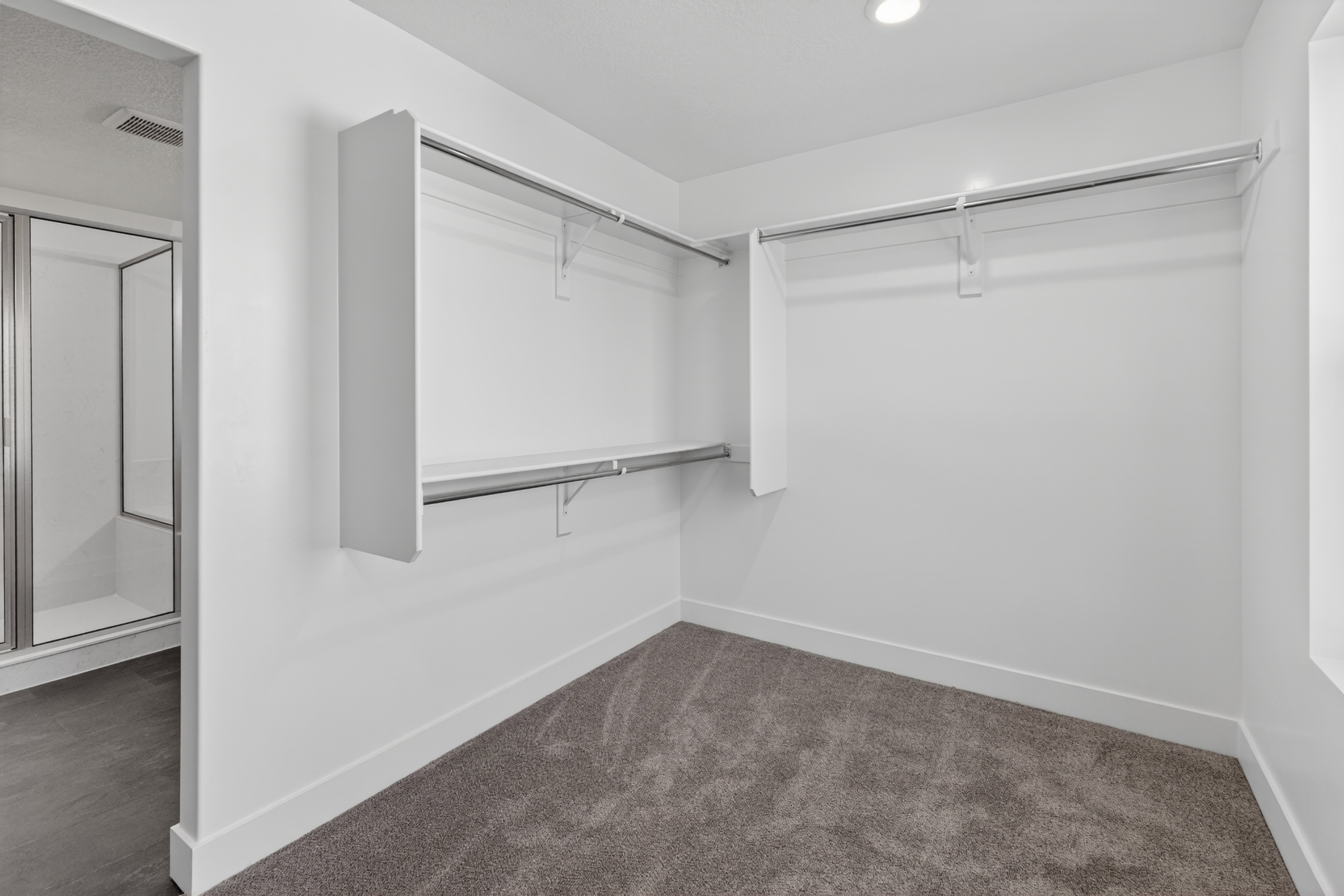 Spacious walk-in closet featuring white walls, gray carpeting, and multiple clothing rods with shelving