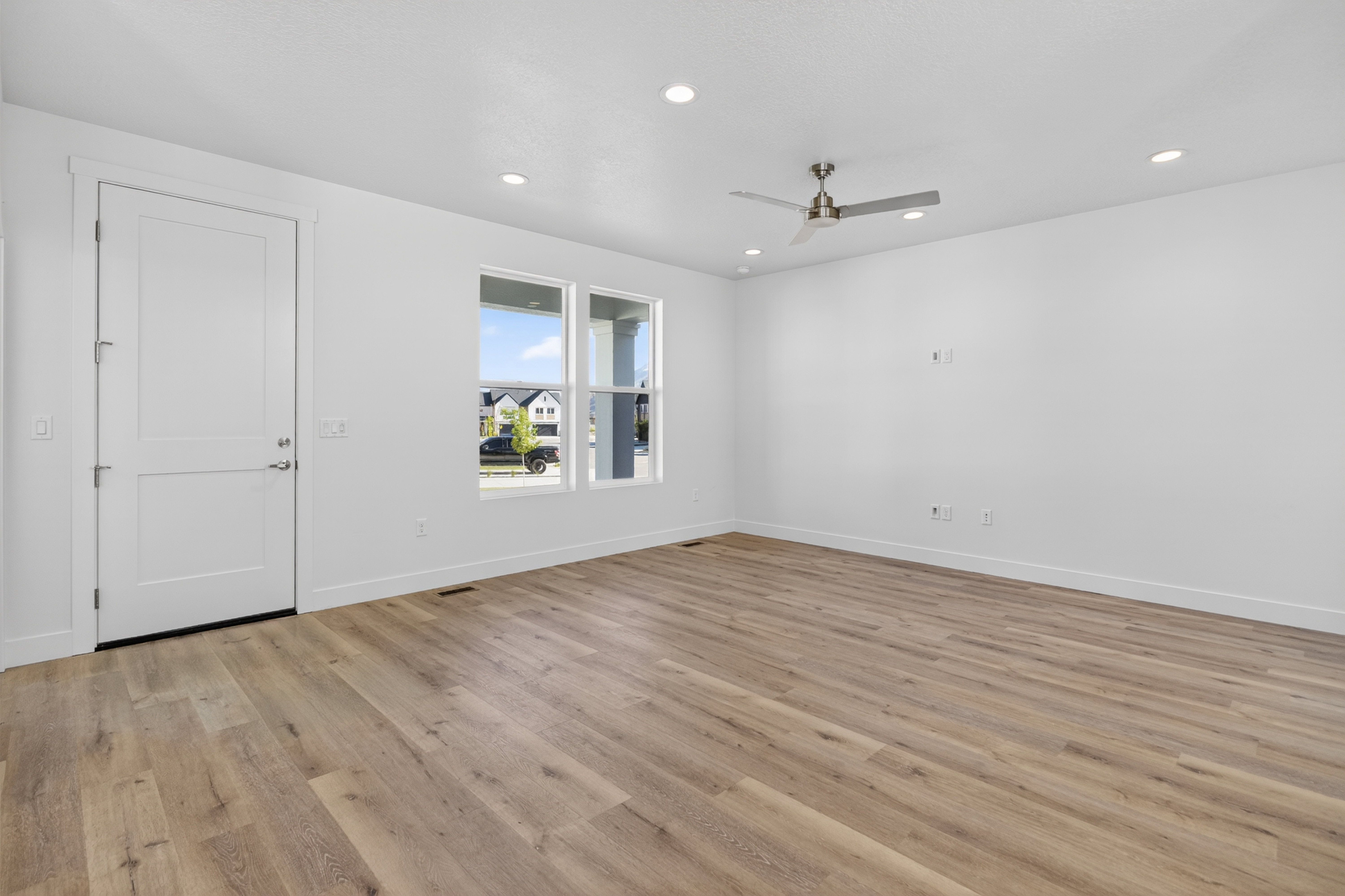 Spacious room featuring wood-finish flooring, white walls, and multiple recessed lights