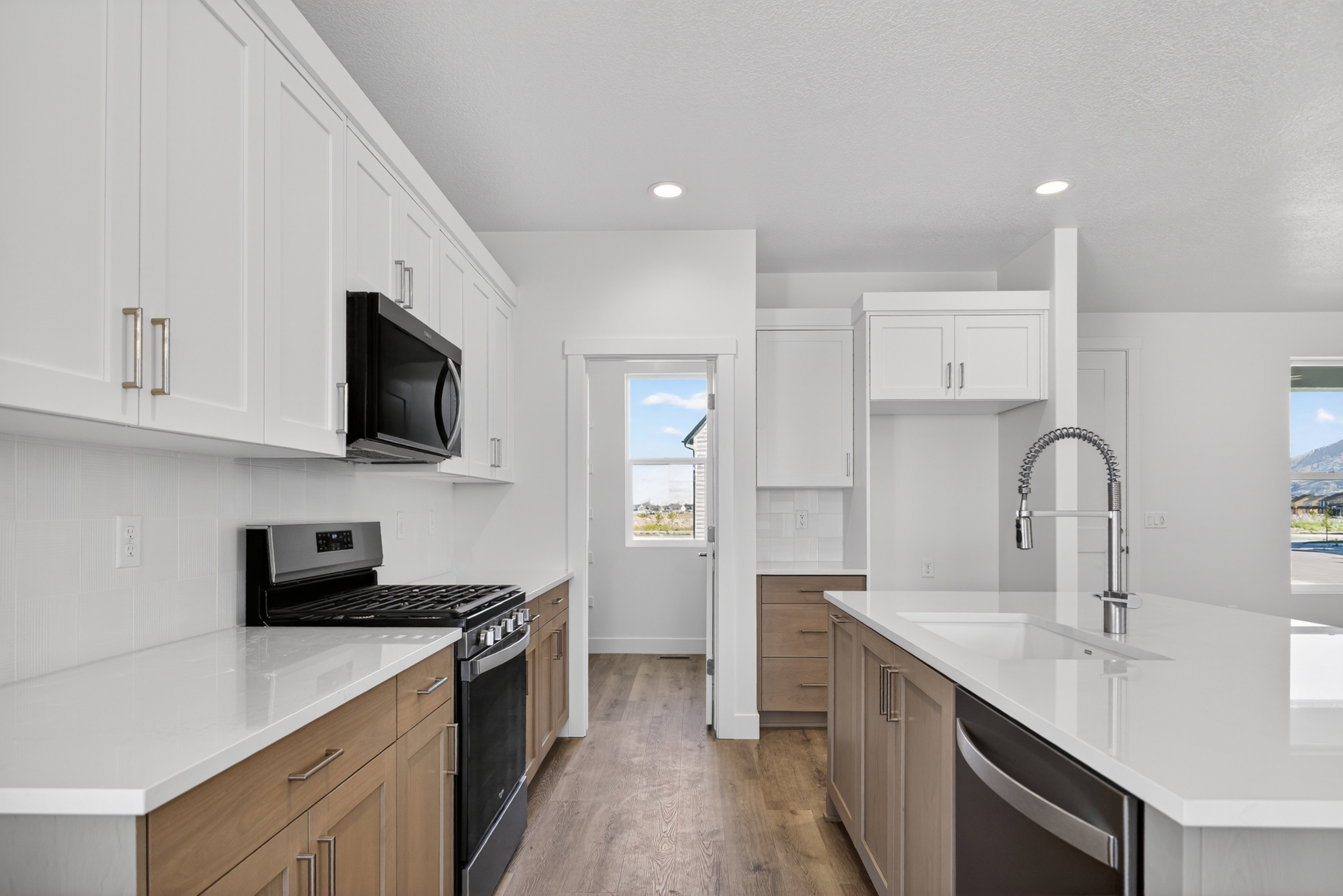 Modern kitchen featuring white upper cabinetry, natural wood-finish lower cabinetry, and light-toned countertops