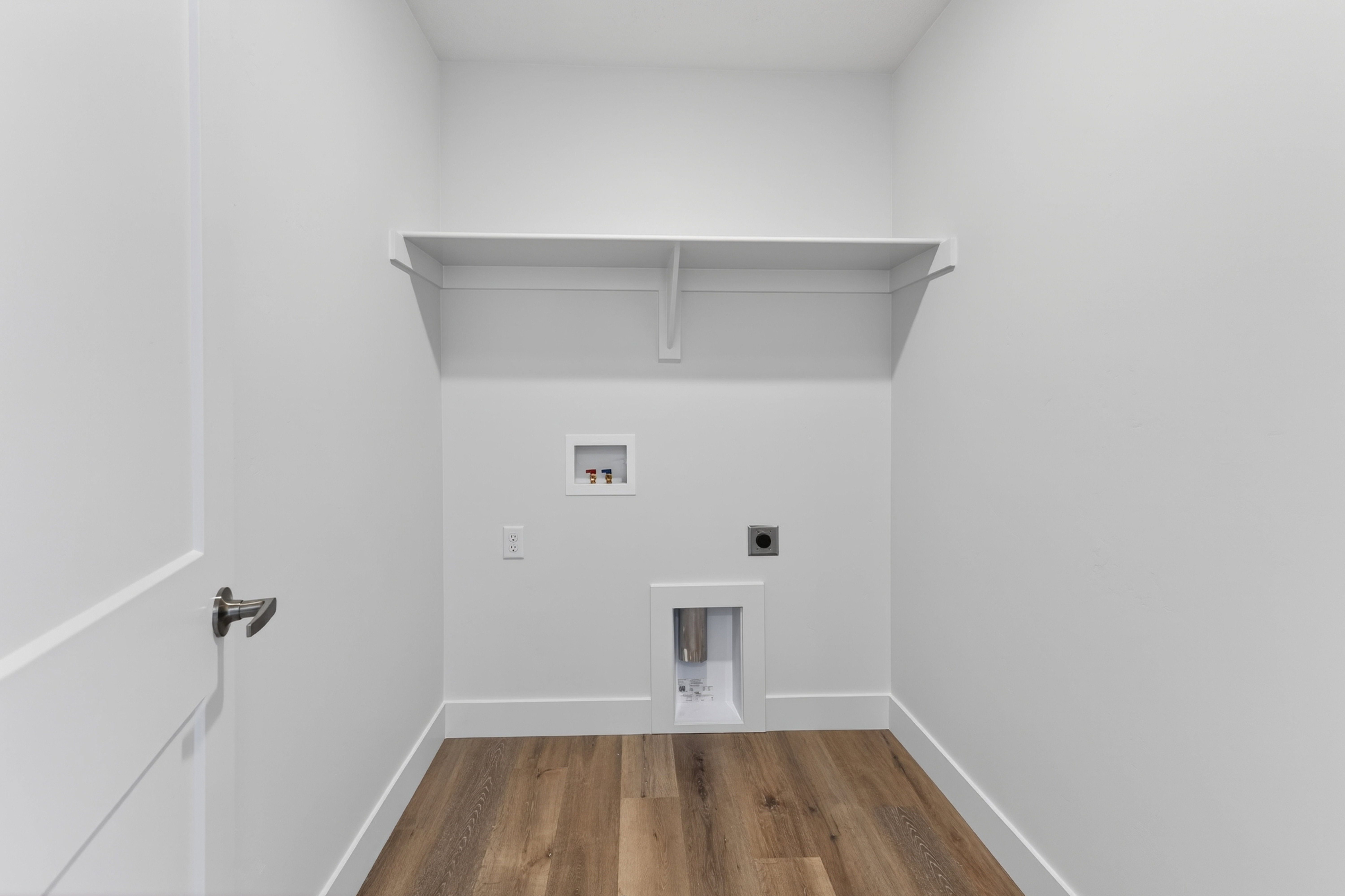 Dedicated utility space featuring wood-finish flooring, a built-in storage shelf, and crisp white walls