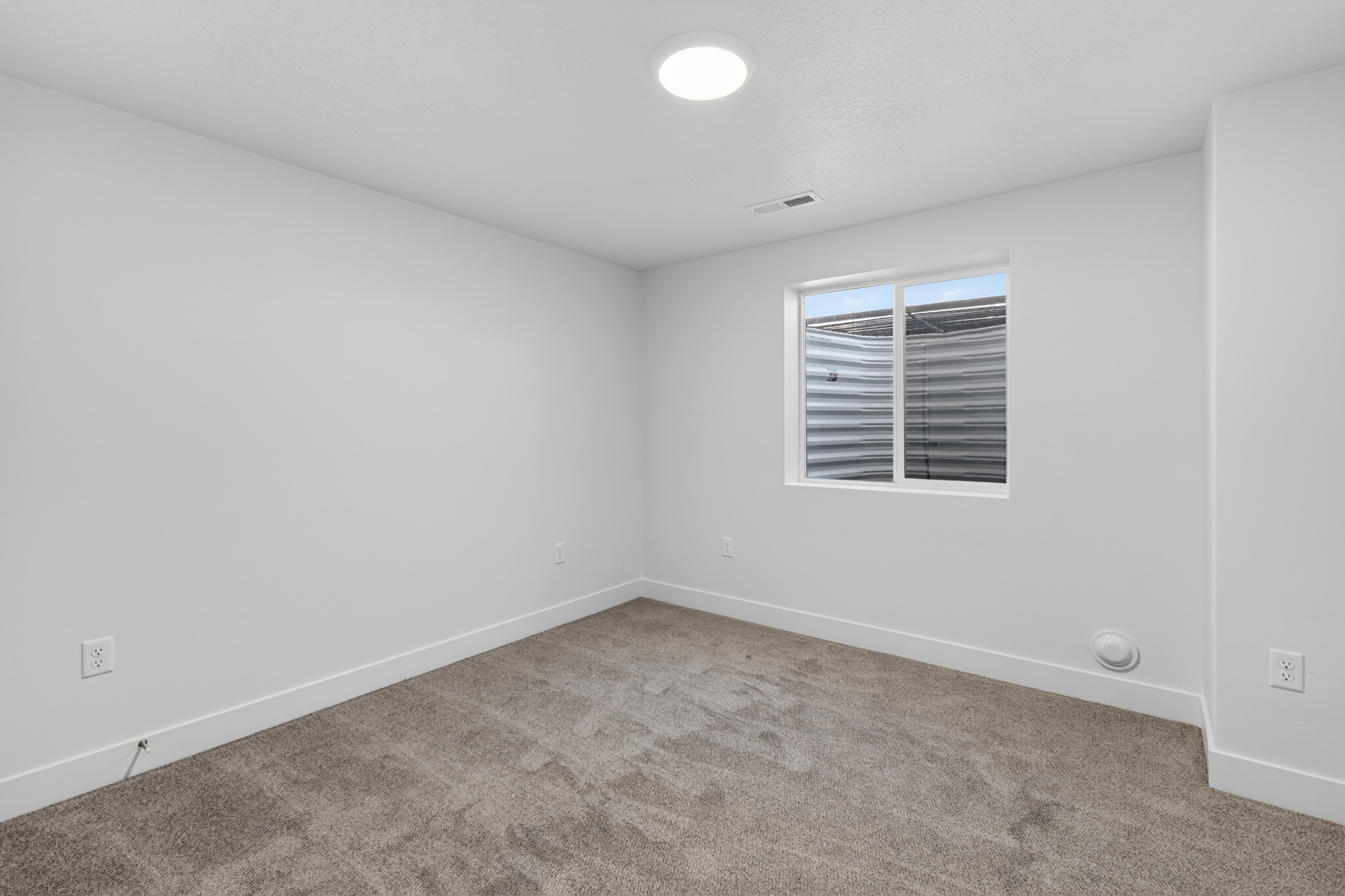 Recessed window featuring a corrugated metal window well, light gray carpeting, crisp white walls, and a circular flush-mount ceiling light