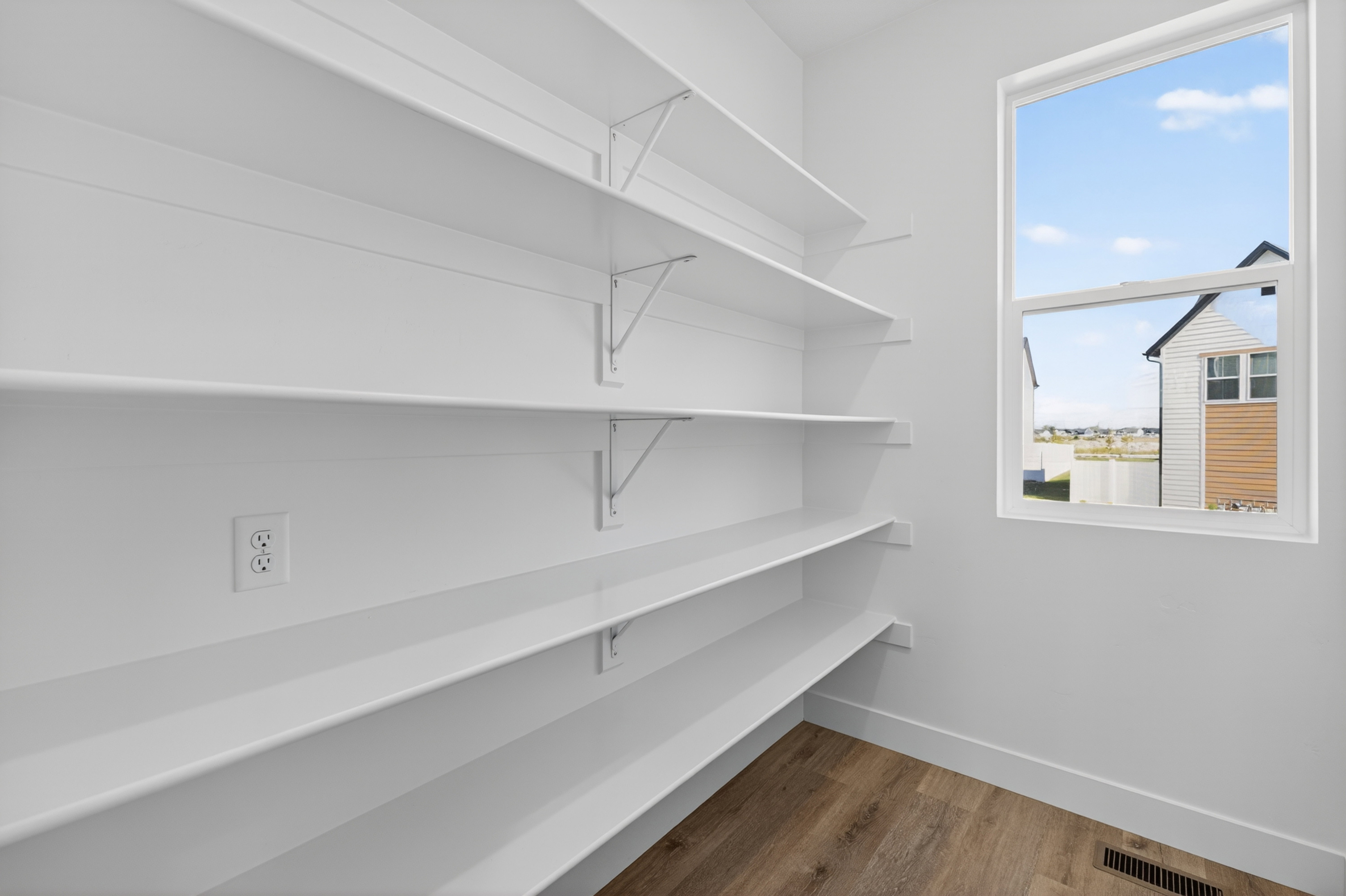 Spacious pantry featuring extensive shelving, wood-finish flooring, a white trim window, and an electrical outlet