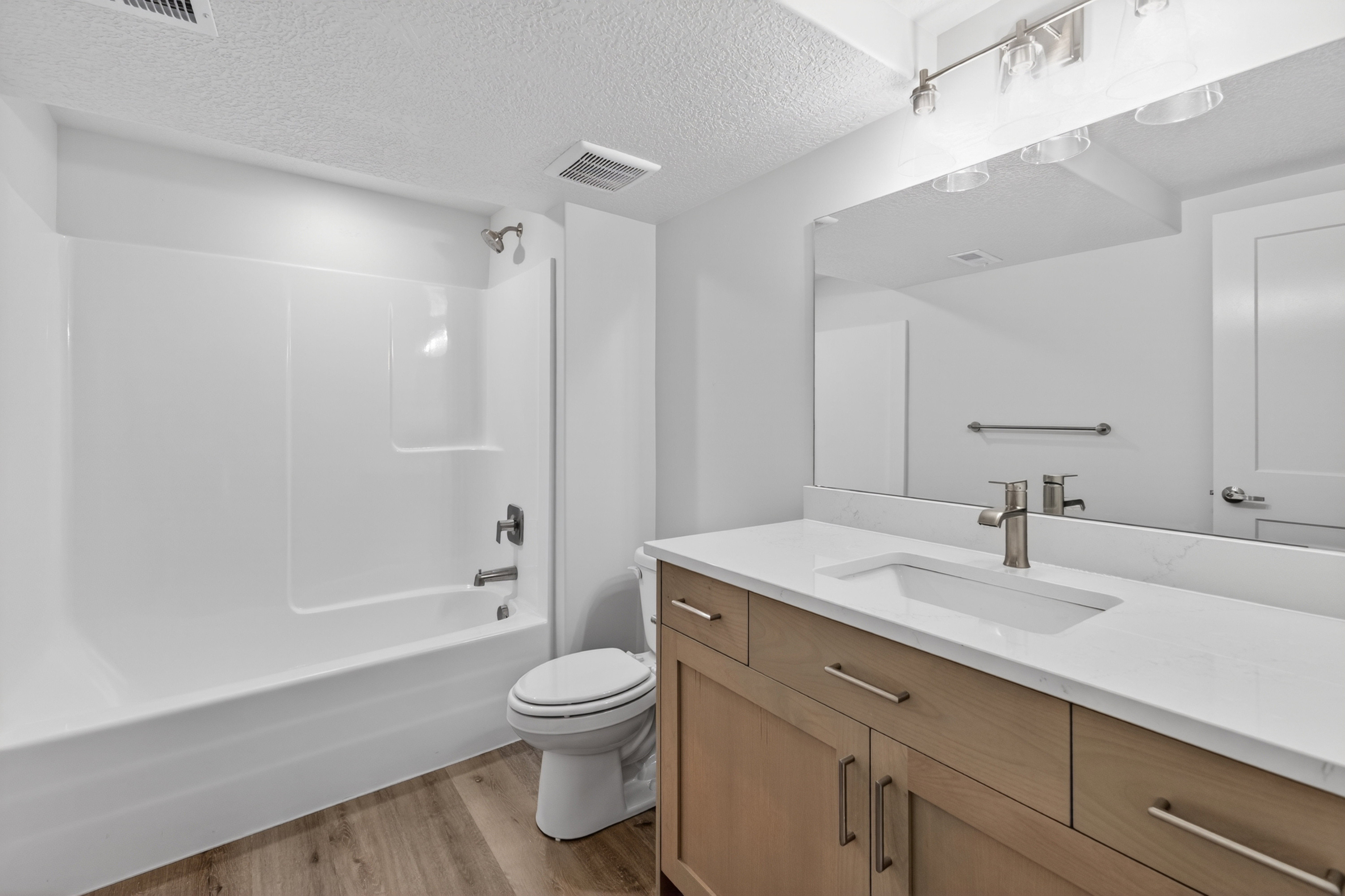Contemporary bathroom featuring a light wood-finish vanity with an integrated sink, white countertop, and brushed nickel hardware