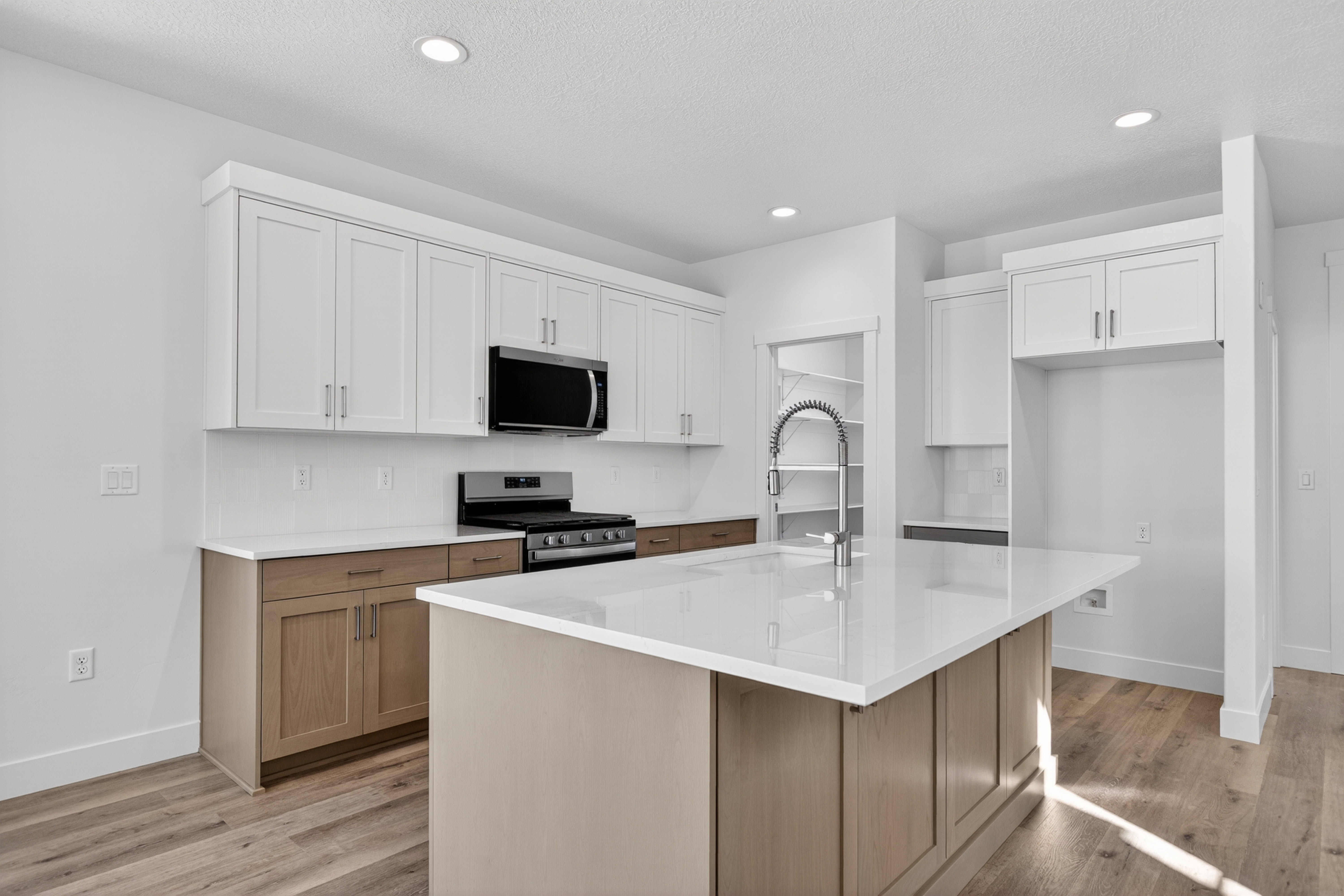 Kitchen featuring a large island with a gooseneck faucet, white countertops, two-tone cabinetry, stainless steel appliances, and wood-finish flooring