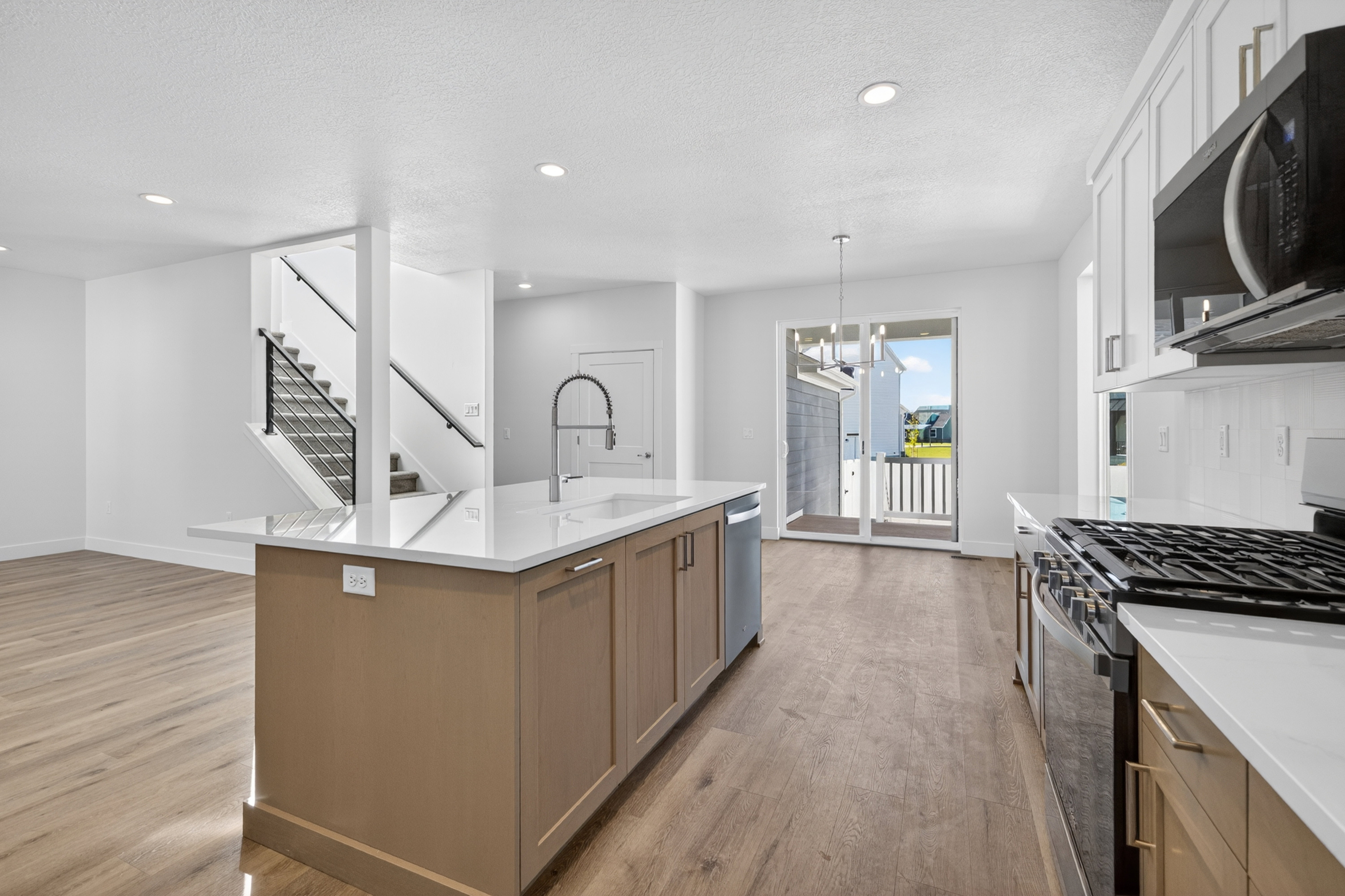 Spacious kitchen featuring a large island with sink, white quartz countertops, wood-finish flooring, white cabinetry, and stainless steel appliances