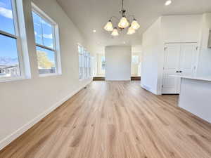 Spacious open-concept room featuring wood-finish flooring, numerous windows, and a multi-bulb chandelier