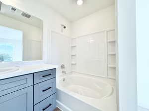 Bathroom featuring a built-in tub with tile surround, integrated shelving, an expansive wall mirror, and a vanity with a light-colored countertop and dark hardware