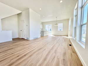 Expansive open-concept living area featuring wood-finish flooring, abundant natural light from multiple windows, recessed lighting, and a contemporary chandelier
