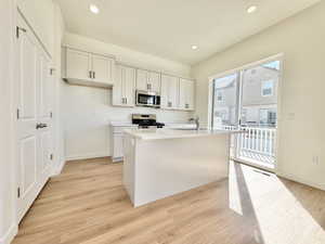 Kitchen featuring white cabinetry, a central island with a sink, stainless steel appliances, light wood-finish flooring, and recessed lighting