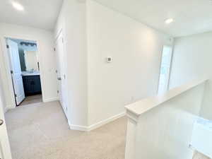 Carpeted hallway featuring white walls, white trim, recessed lighting, and a partial staircase railing