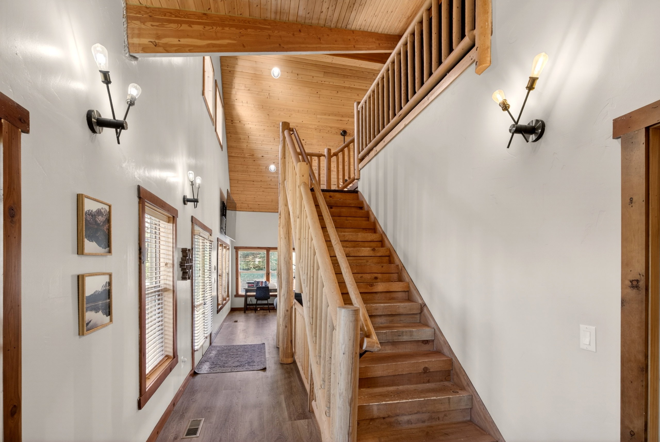 Expansive entryway featuring wood-finish flooring, a prominent wooden staircase with log newel posts, and decorative wall sconces