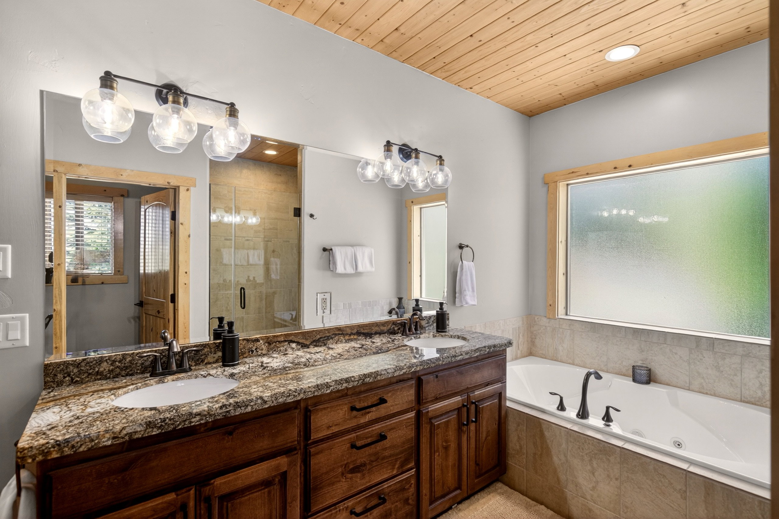 Dual vanity with granite countertop and undermount sinks, accompanied by a built-in jetted tub