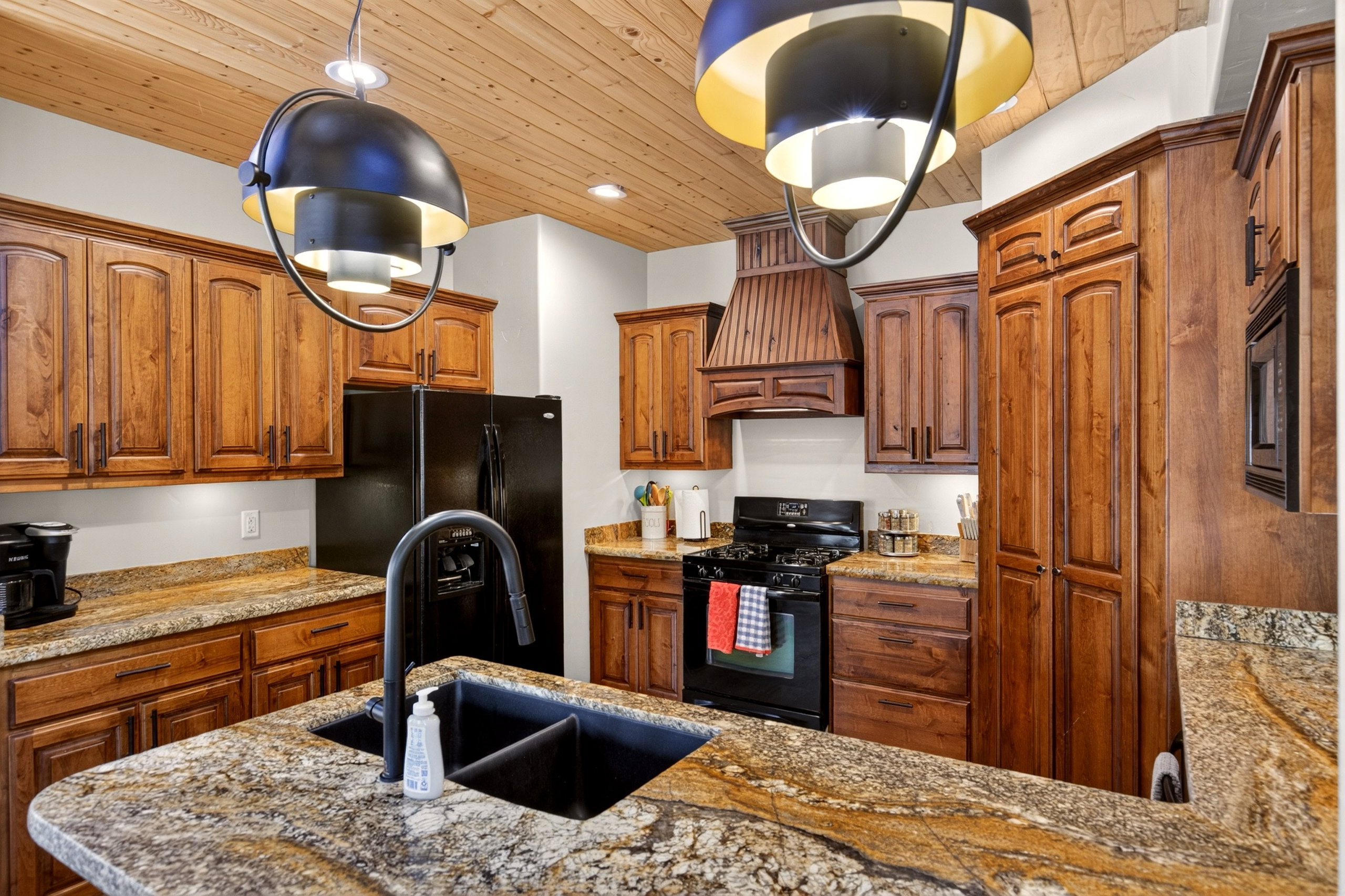 Kitchen featuring a wood-finish plank ceiling, granite countertops, wood cabinetry, a black appliance suite, and an island with an undermount sink